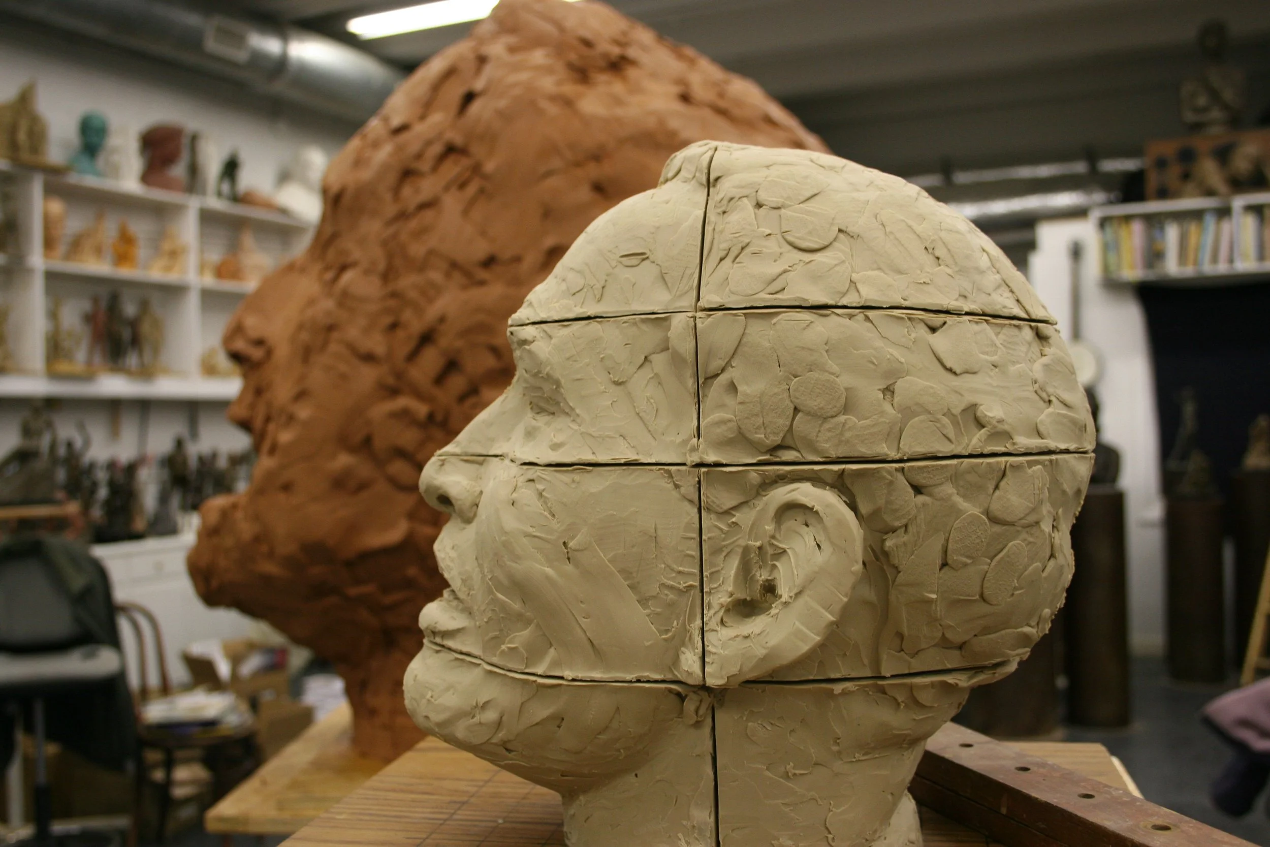 Clay sculpture of a human head in progress, with a profile view, featuring textured surface and layered construction, in an art studio.
