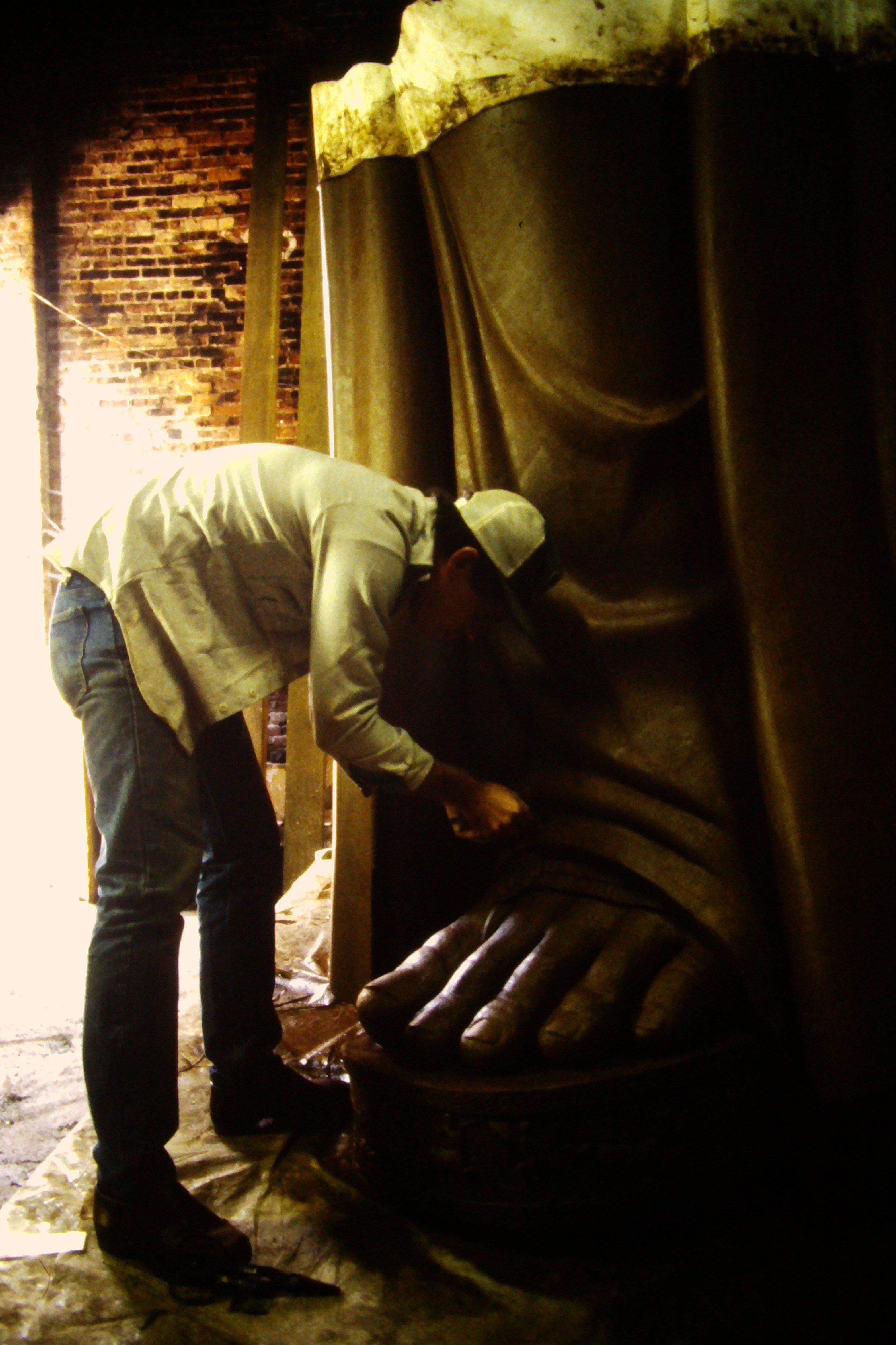 A person in a light jacket and cap working on a large sculpture of Athena Parthenos in Parthenon Museum Nashville. 