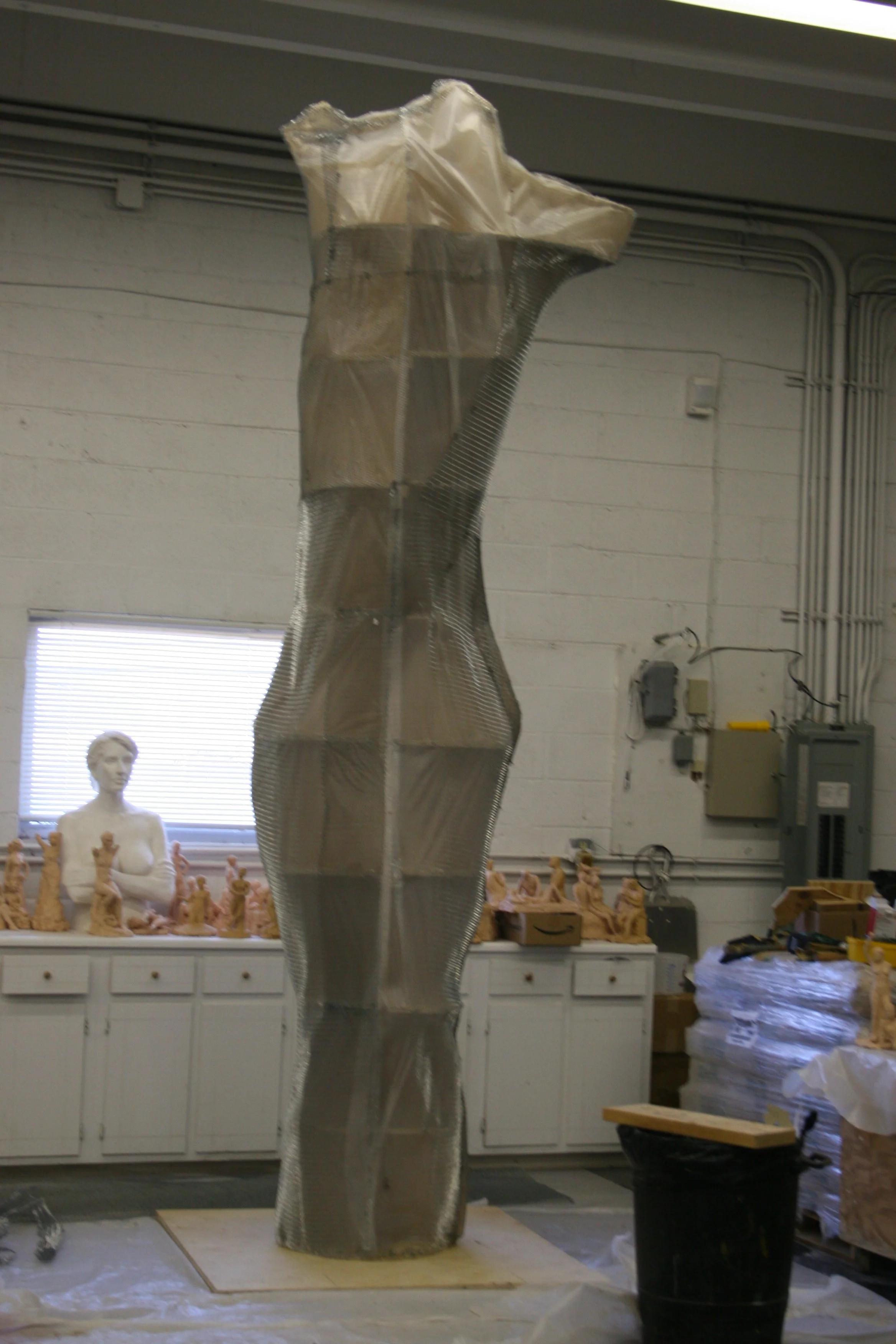 A metallic wrapped sculpture in an artist's studio, with sculptures and statues in the background.