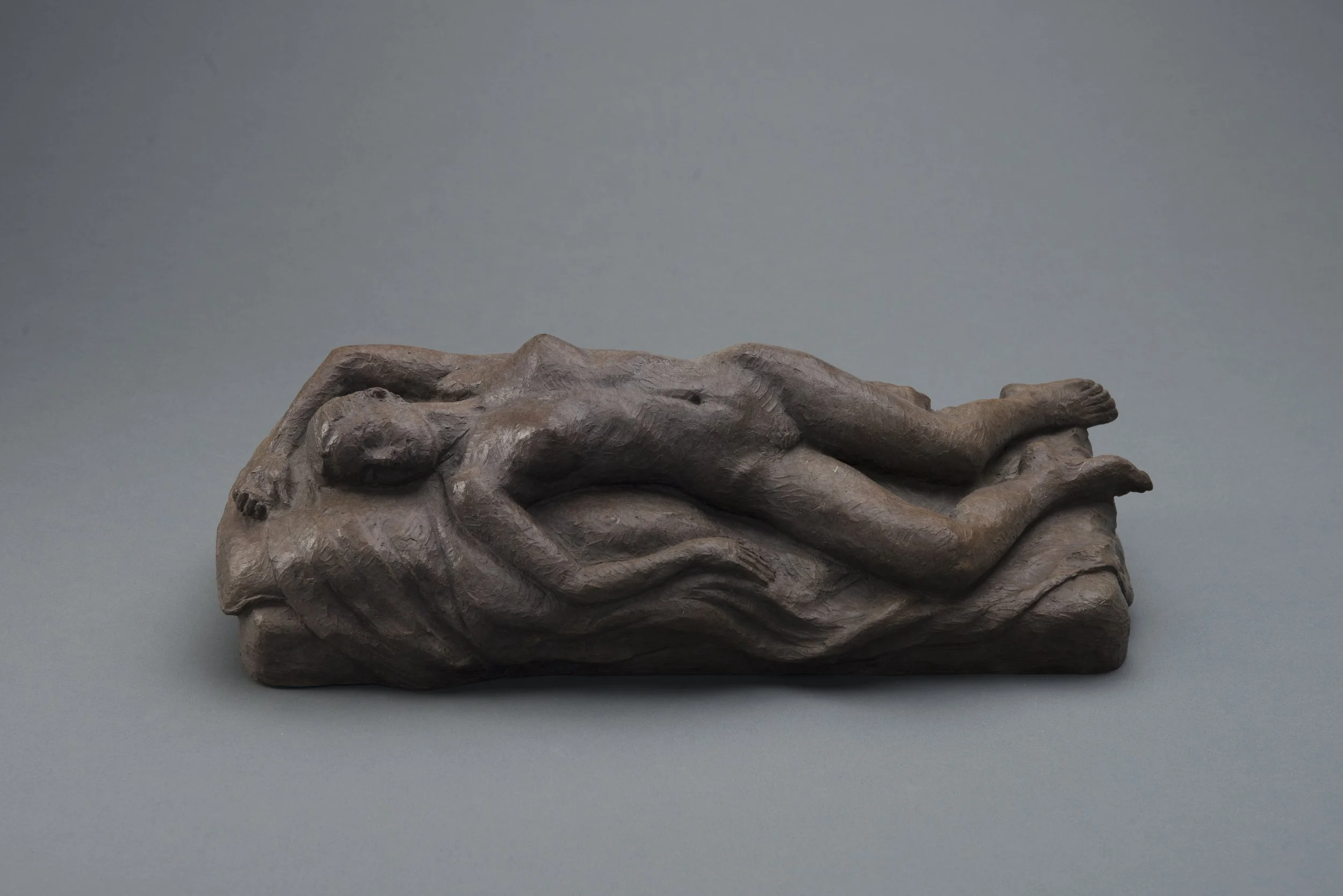 Bronze sculpture of a resting woman lying on her side with her eyes closed, on a gray background.