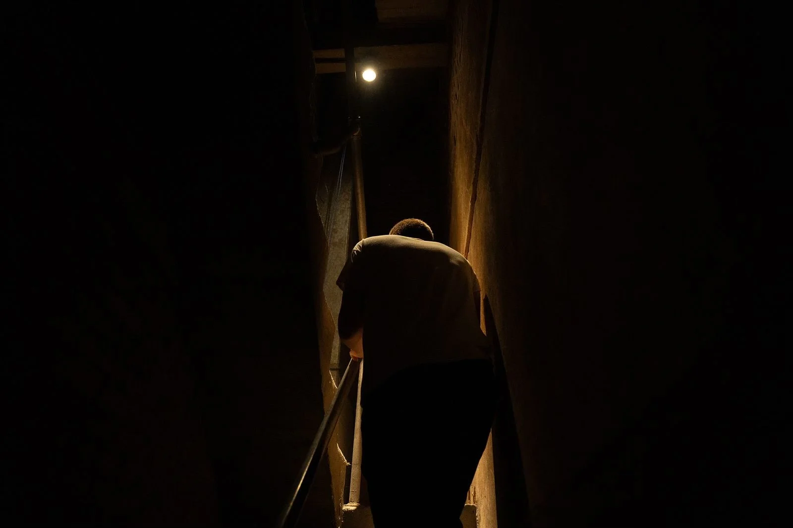 Person climbing a dimly lit narrow staircase with warm light at the top.