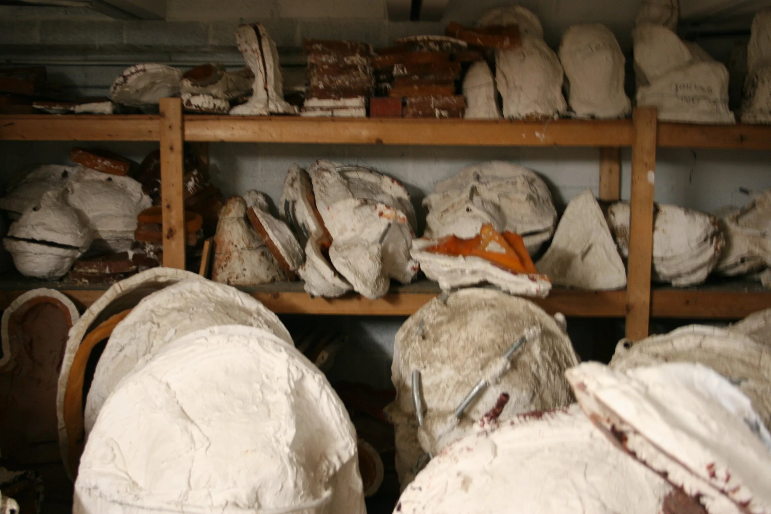 Shelves filled with molds, some broken, stored in a workshop or storage area.