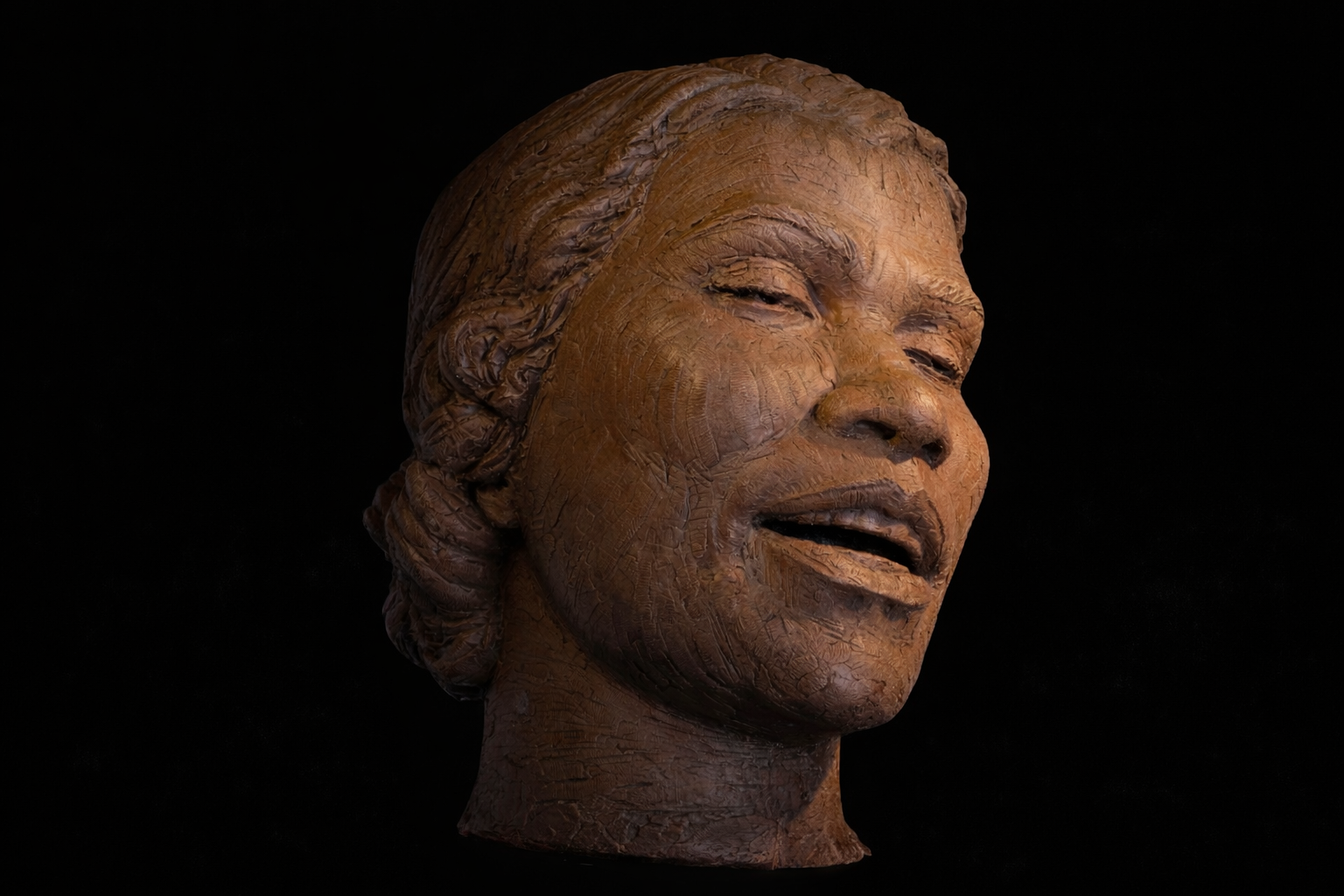 A wooden sculpture of a smiling woman's face with her eyes partially closed, set against a black background.