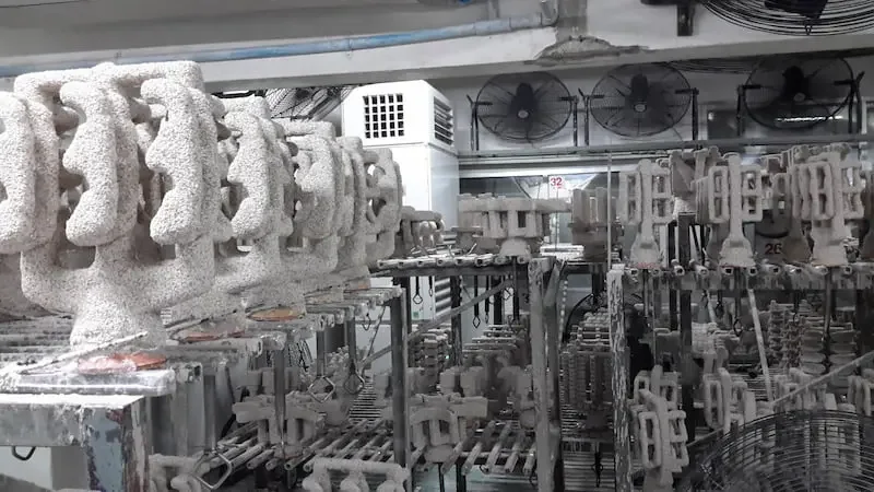Factory conveyor system with multiple metal fixtures and fans in the background.