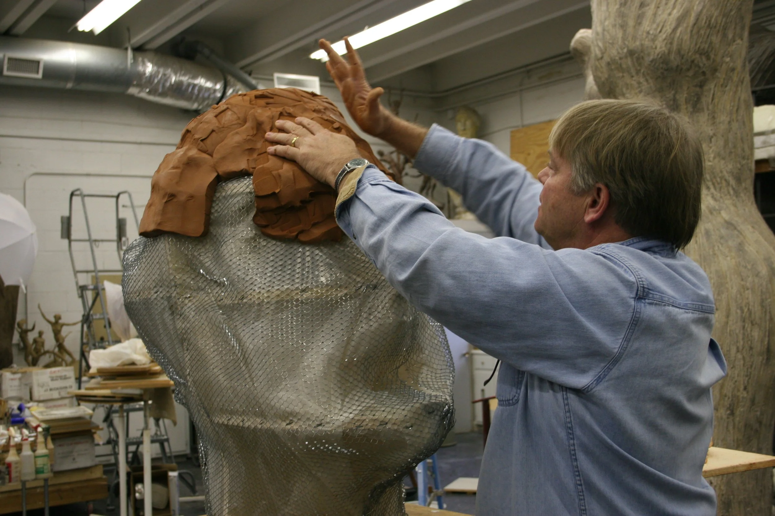 A person working on a large sculpture in an art studio, using their hands to shape the clay surface of the sculpture.