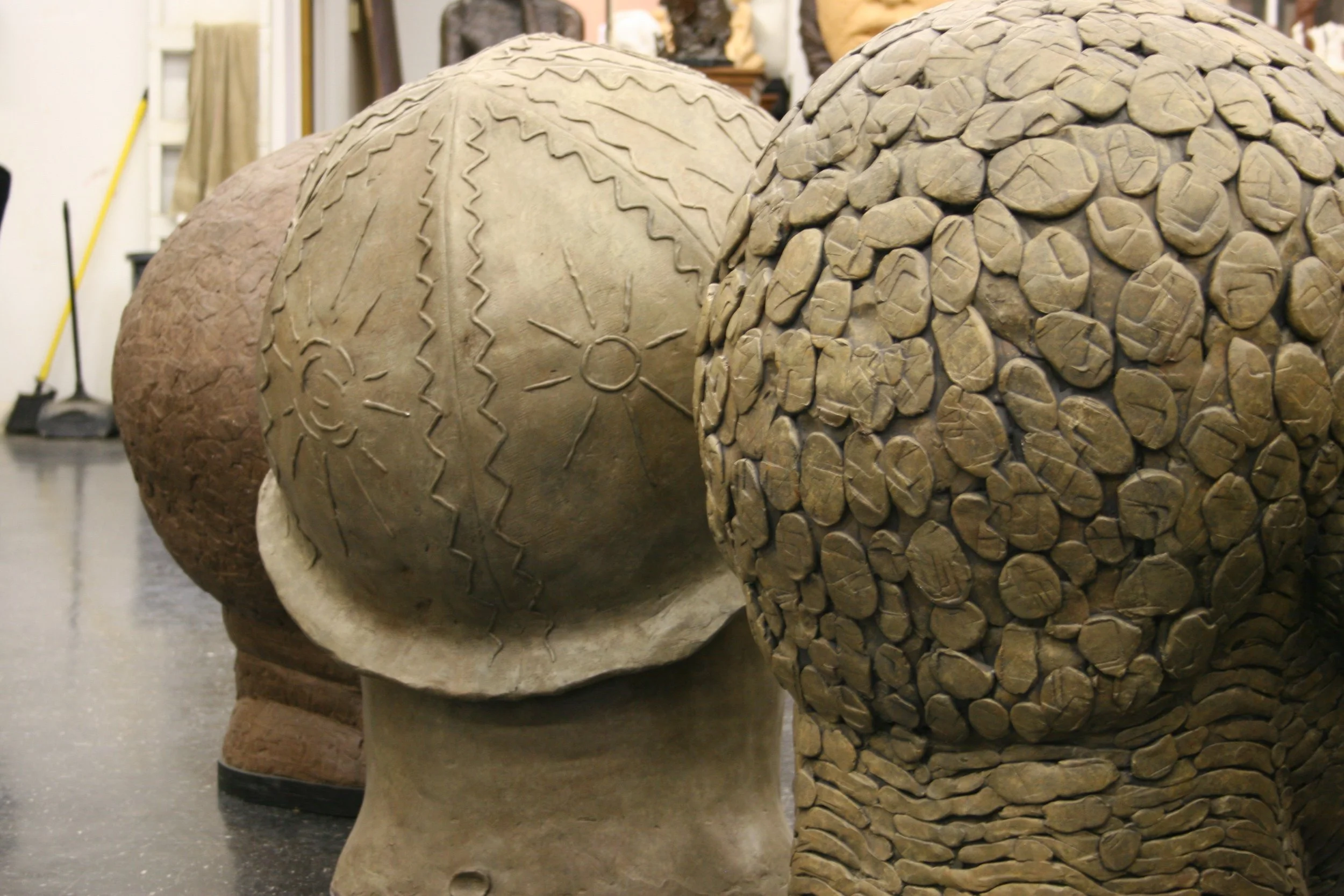 Three carved sculptures with different textures and patterns, likely representing heads or busts, displayed in an indoor museum setting.  Cultural Heroes