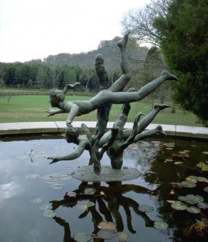 Sculpture of a girl climbing on a tree branch, situated in a pond with lily pads, outdoors in a park.