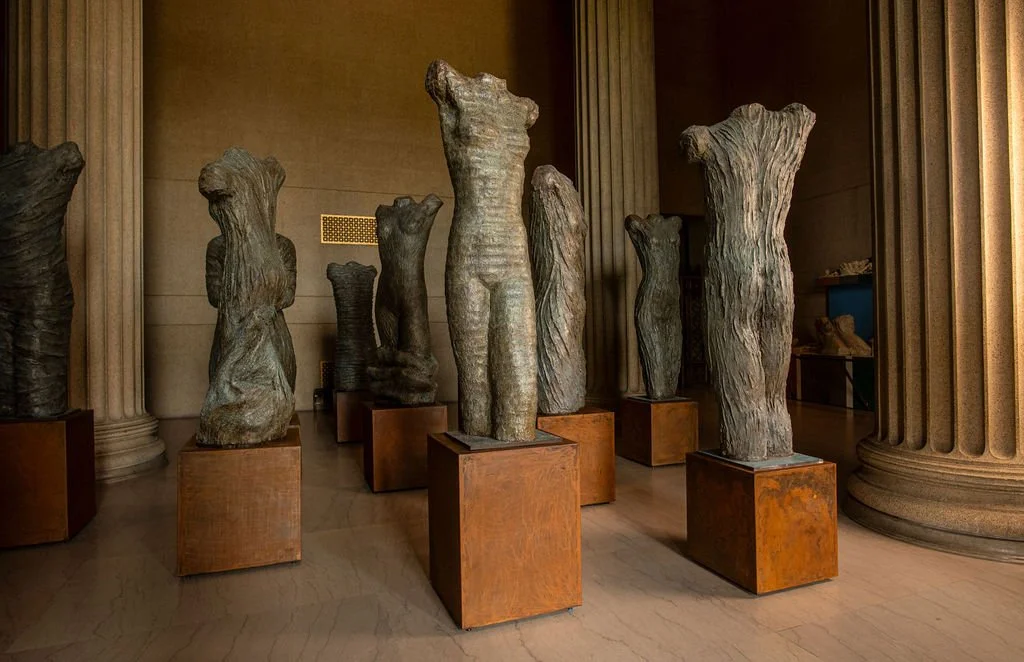 Multiple large, irregularly shaped stone sculptures displayed on wooden pedestals inside a museum with classical columns.