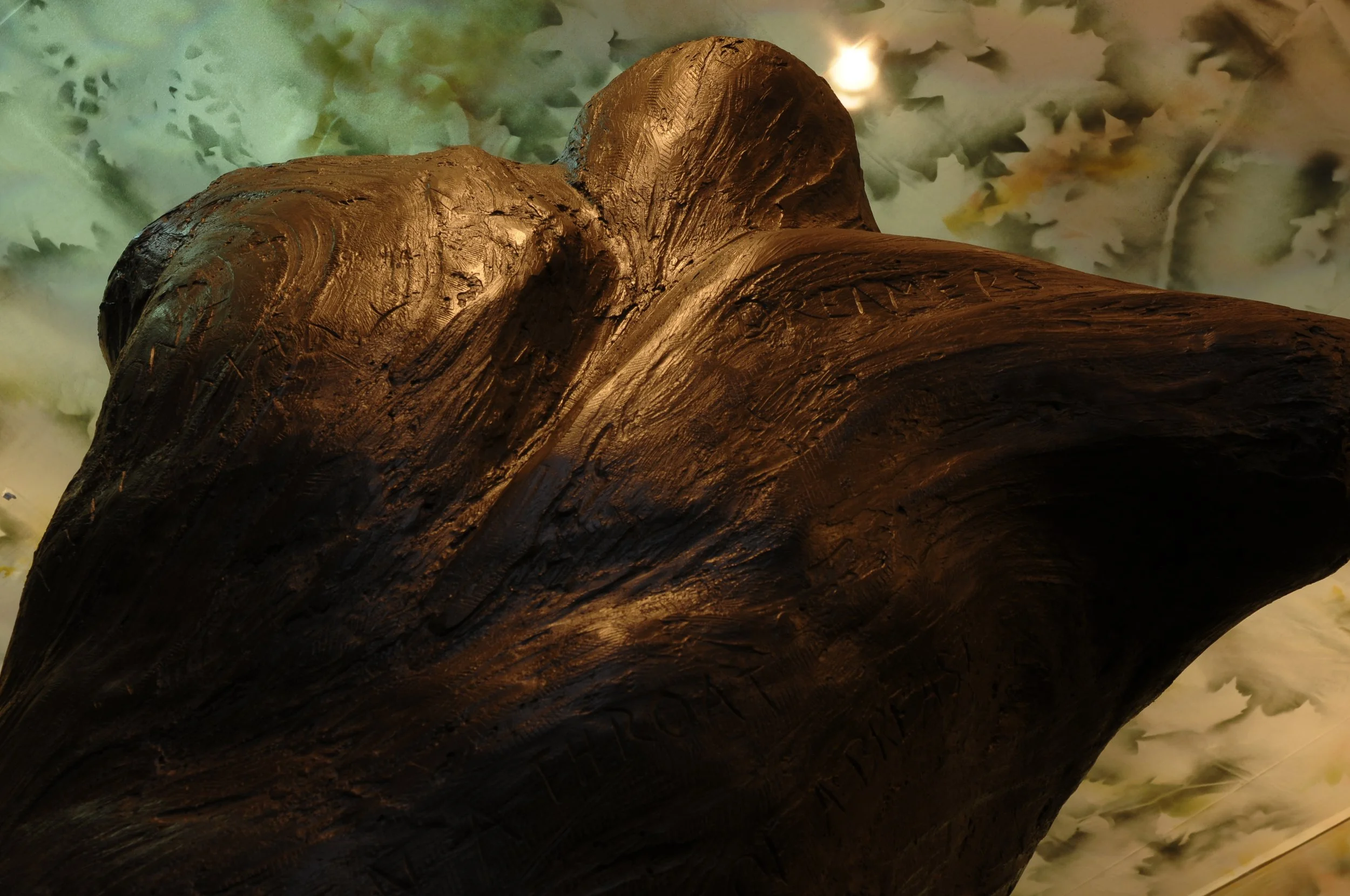 Close-up view of a brown, textured wooden sculpture with a blurred green leafy background. Dream Forest.