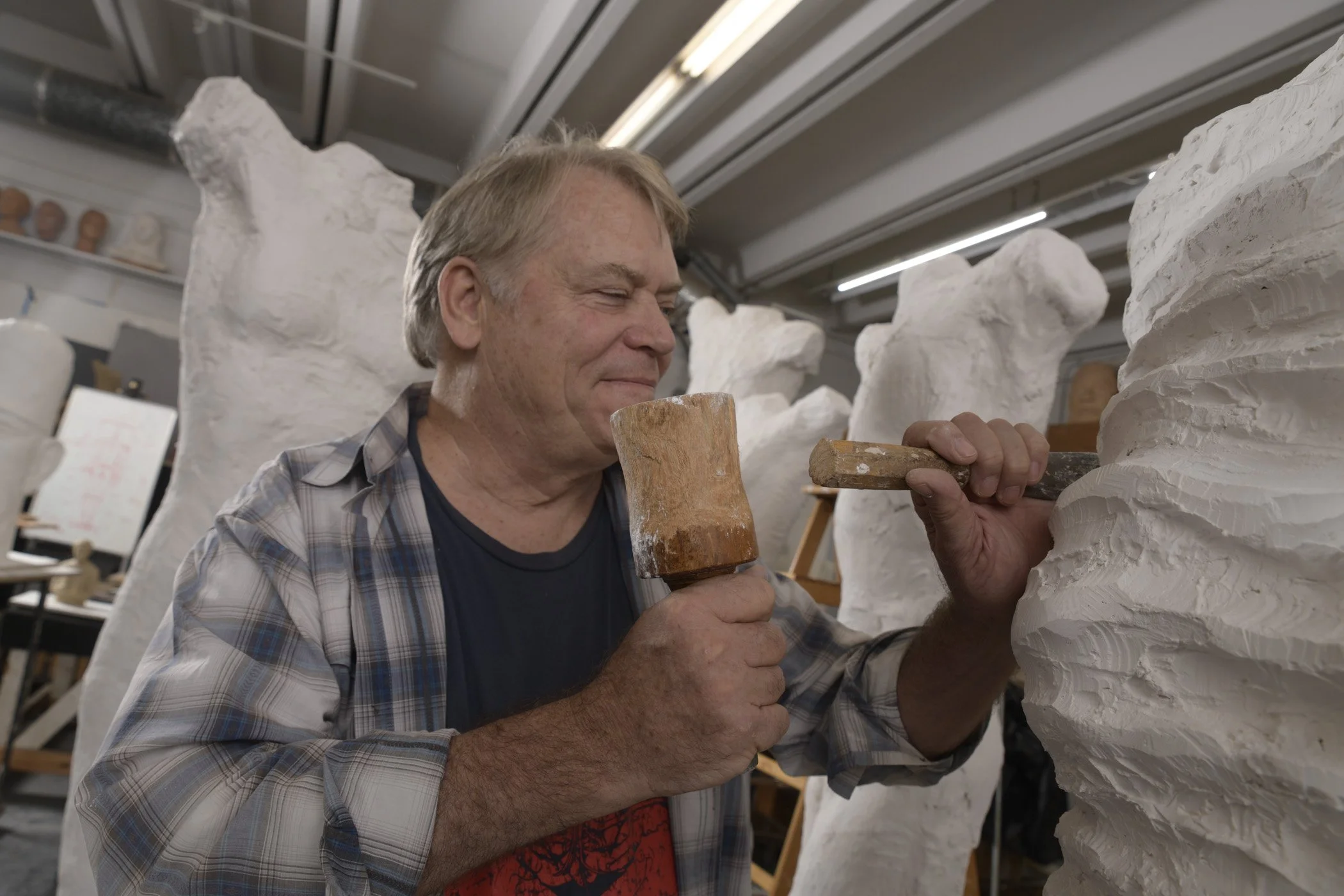 A man sculpting a large white sculpture using tools in an art studio.