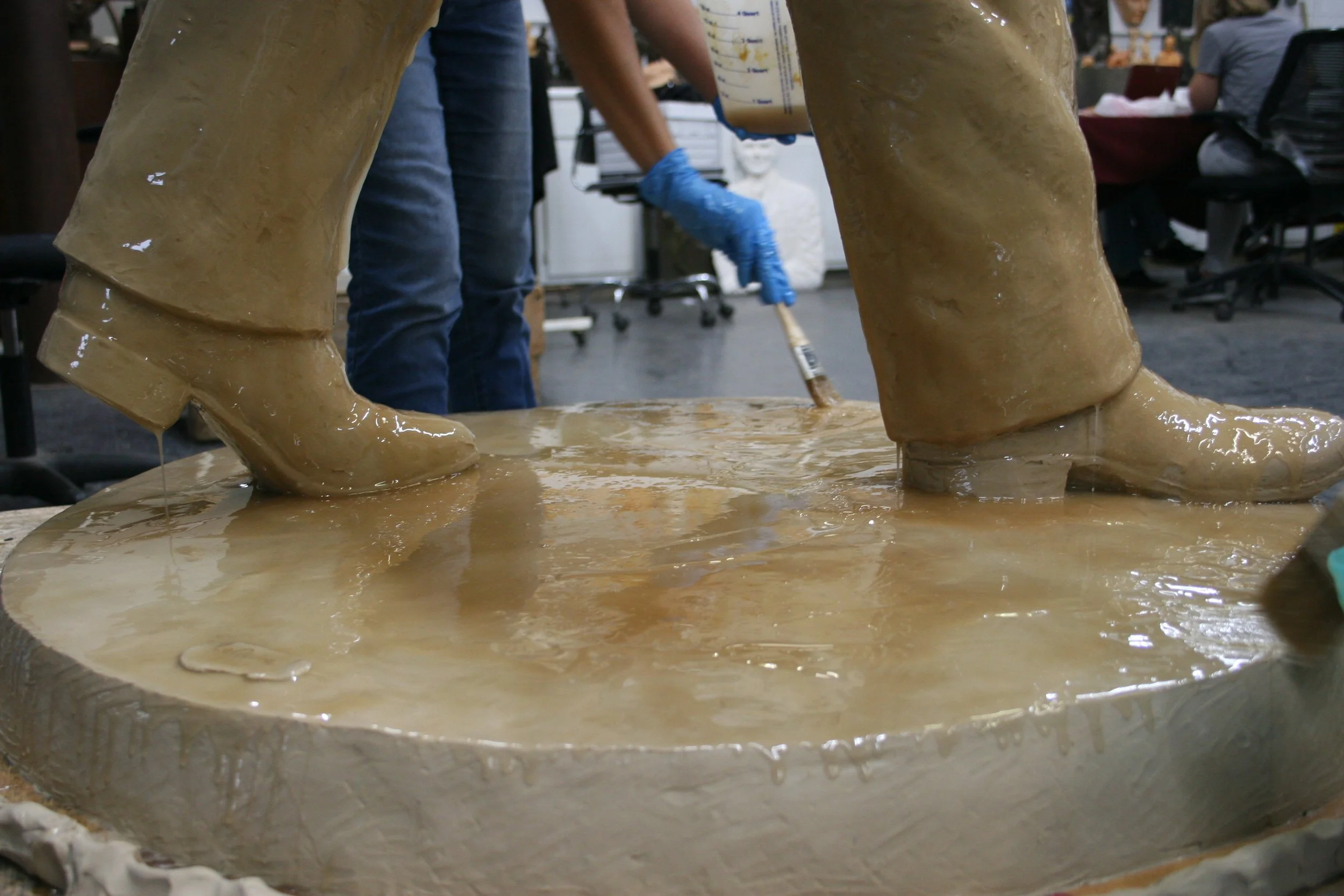 Close-up of an artist pouring brown liquid rubber to make a mold of a clay sculpture.