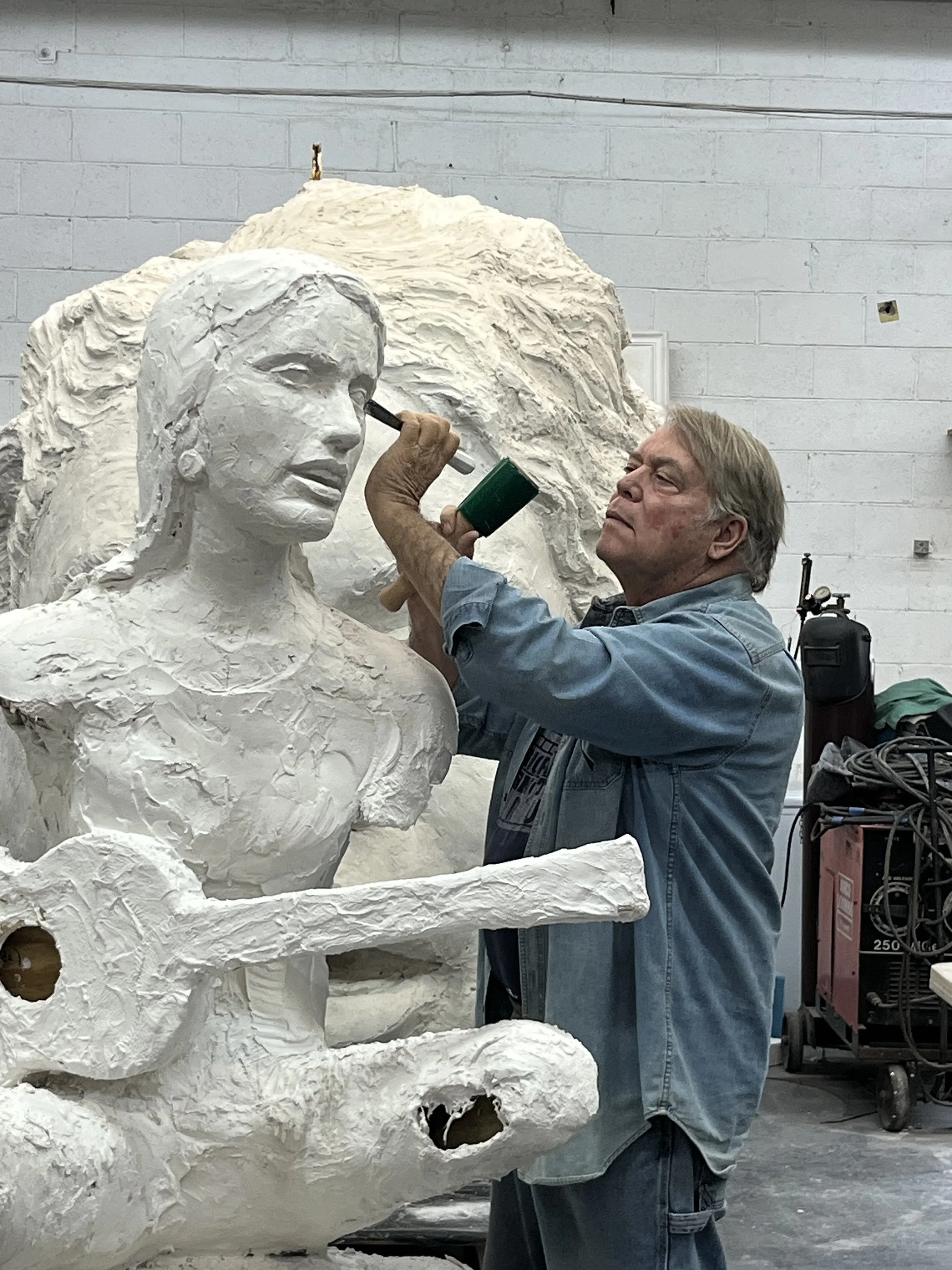 An artist working on a large white sculpture of a woman, possibly a bust, in a workshop.