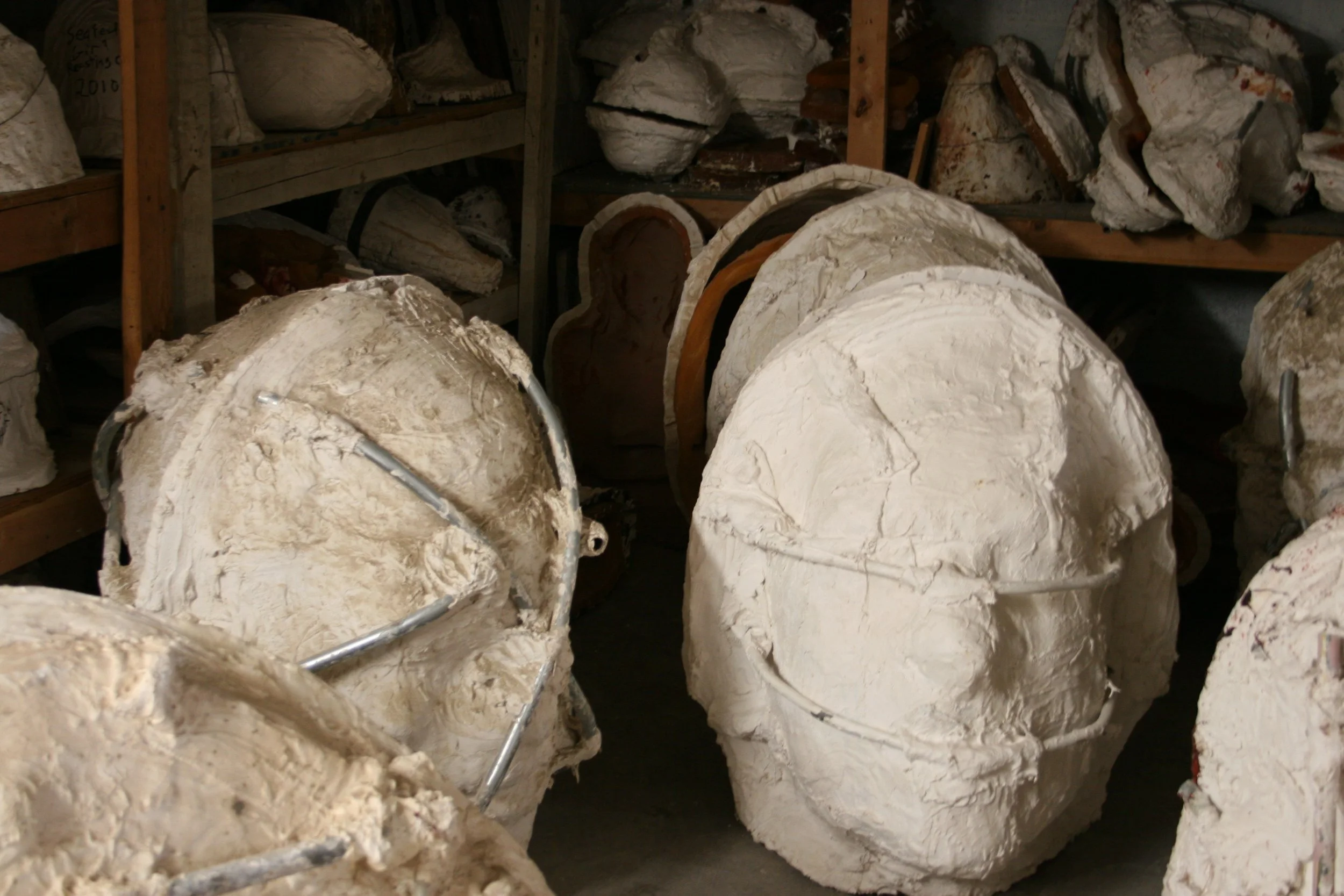 Stacked large pieces of white  sculptural molds stored on wooden shelves.
