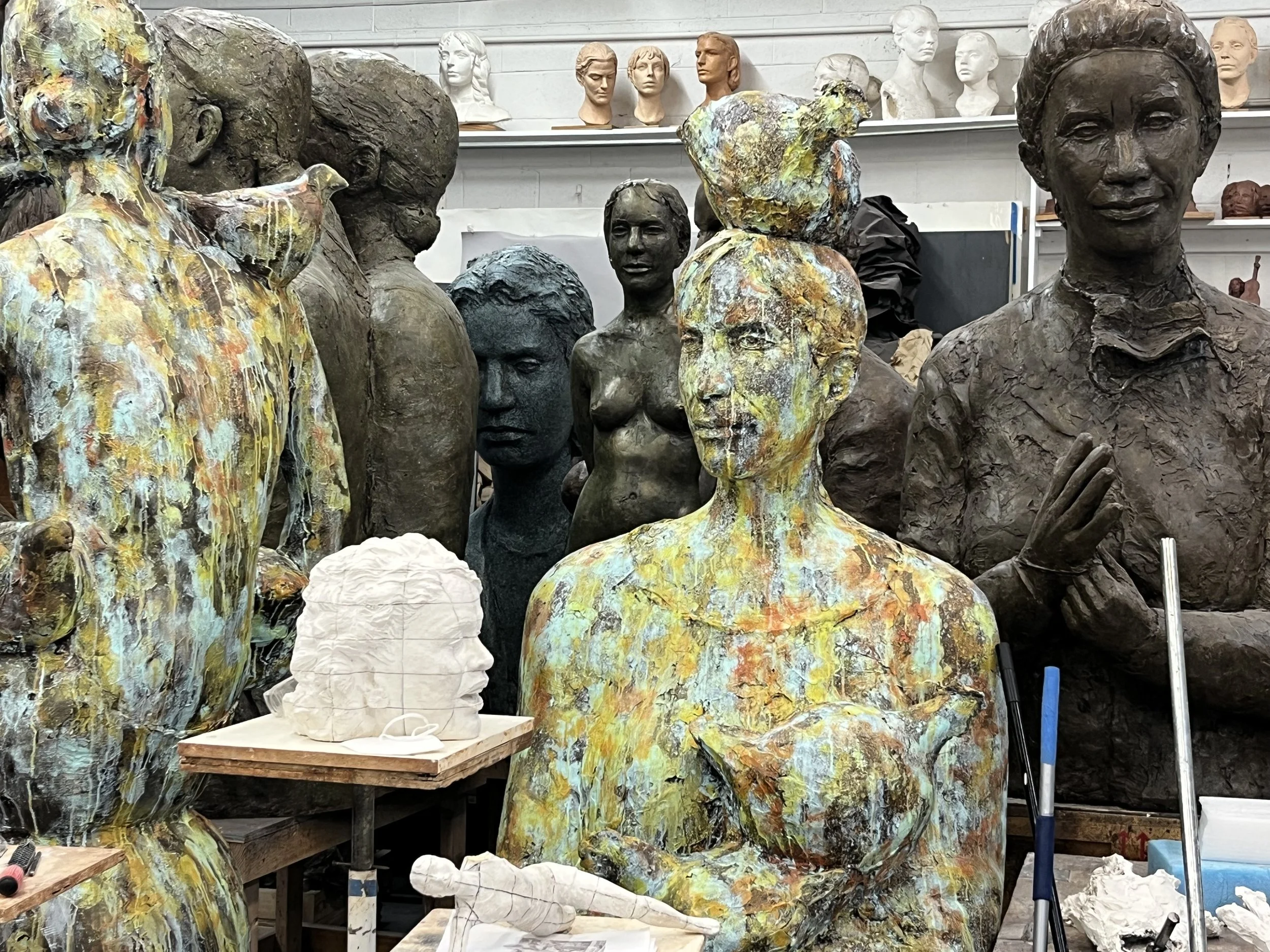 Studio filled with artistic sculptures and busts in various stages of completion, including textured and painted human figures and heads.