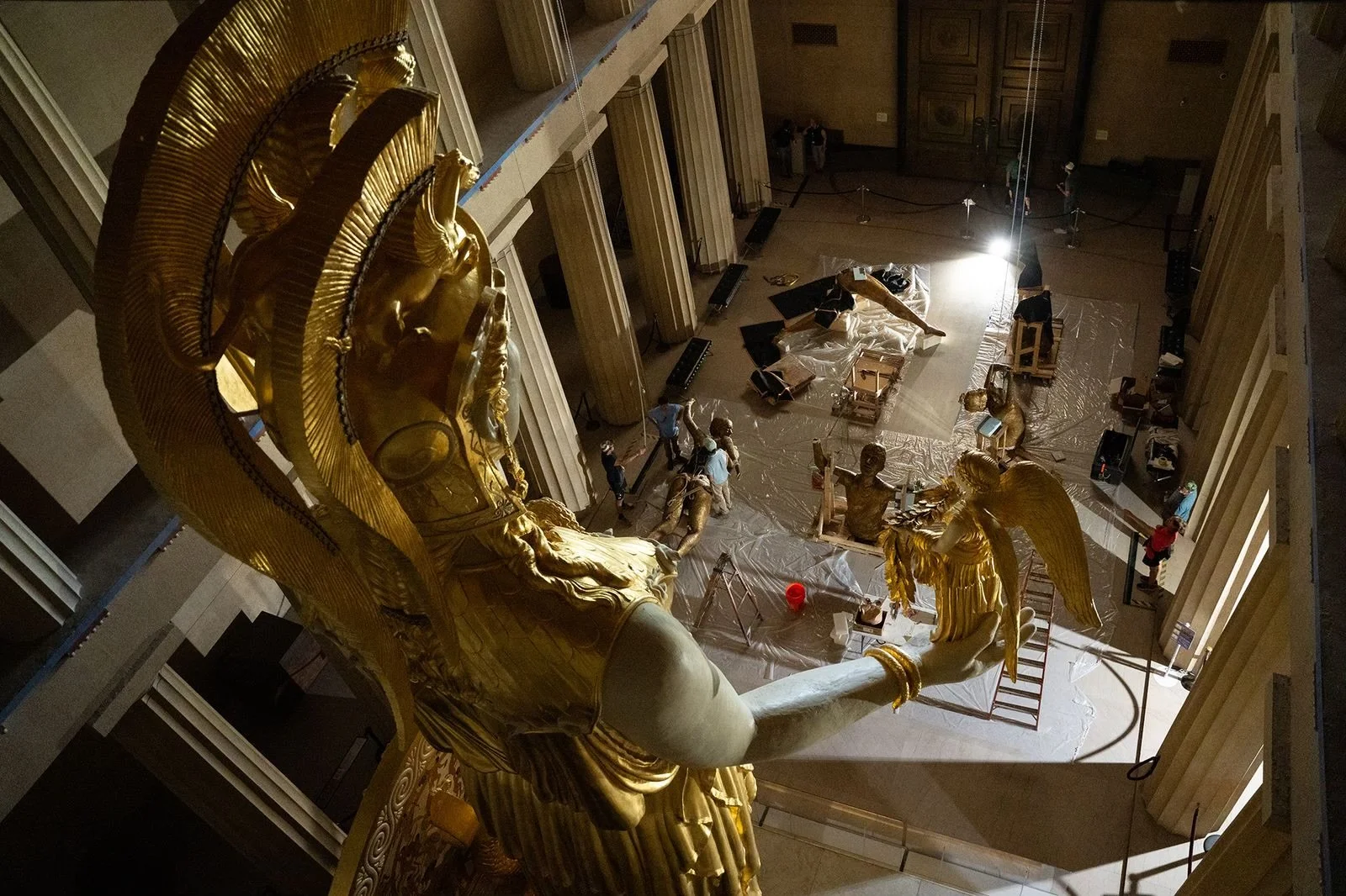 A high-angle view of the gold sculpture of Lady Justice in a building undergoing maintenance, with workers present and tools scattered on the floor. Parthenon Museum and Alan LeQuire and Monumental Figures exhibit. 
