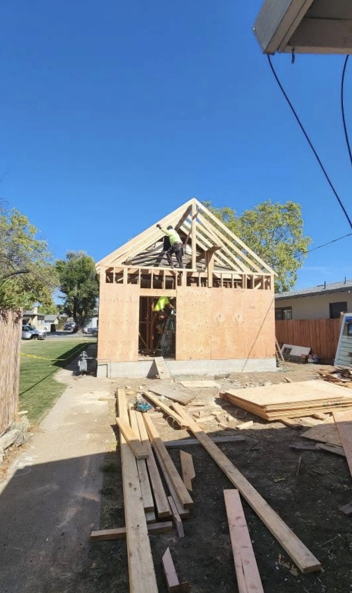 Construction workers building a house with wooden framing under a clear blue sky.