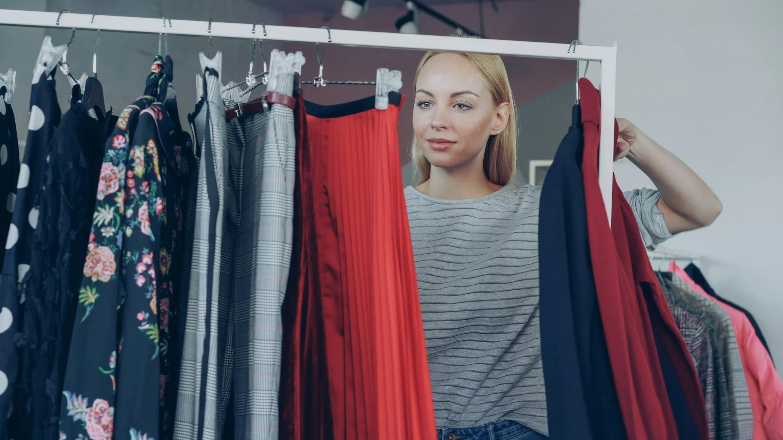 A woman shopping for clothes, looking at a rack of dresses in a store.
