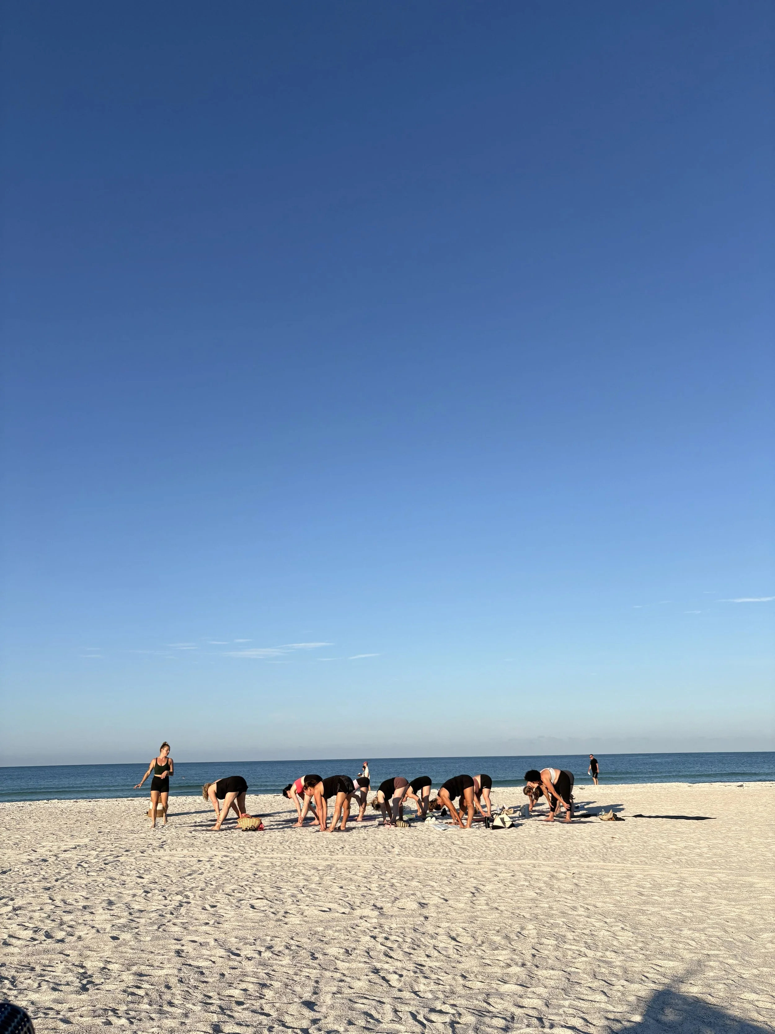 People practicing yoga on a sandy beach under a clear blue sky.