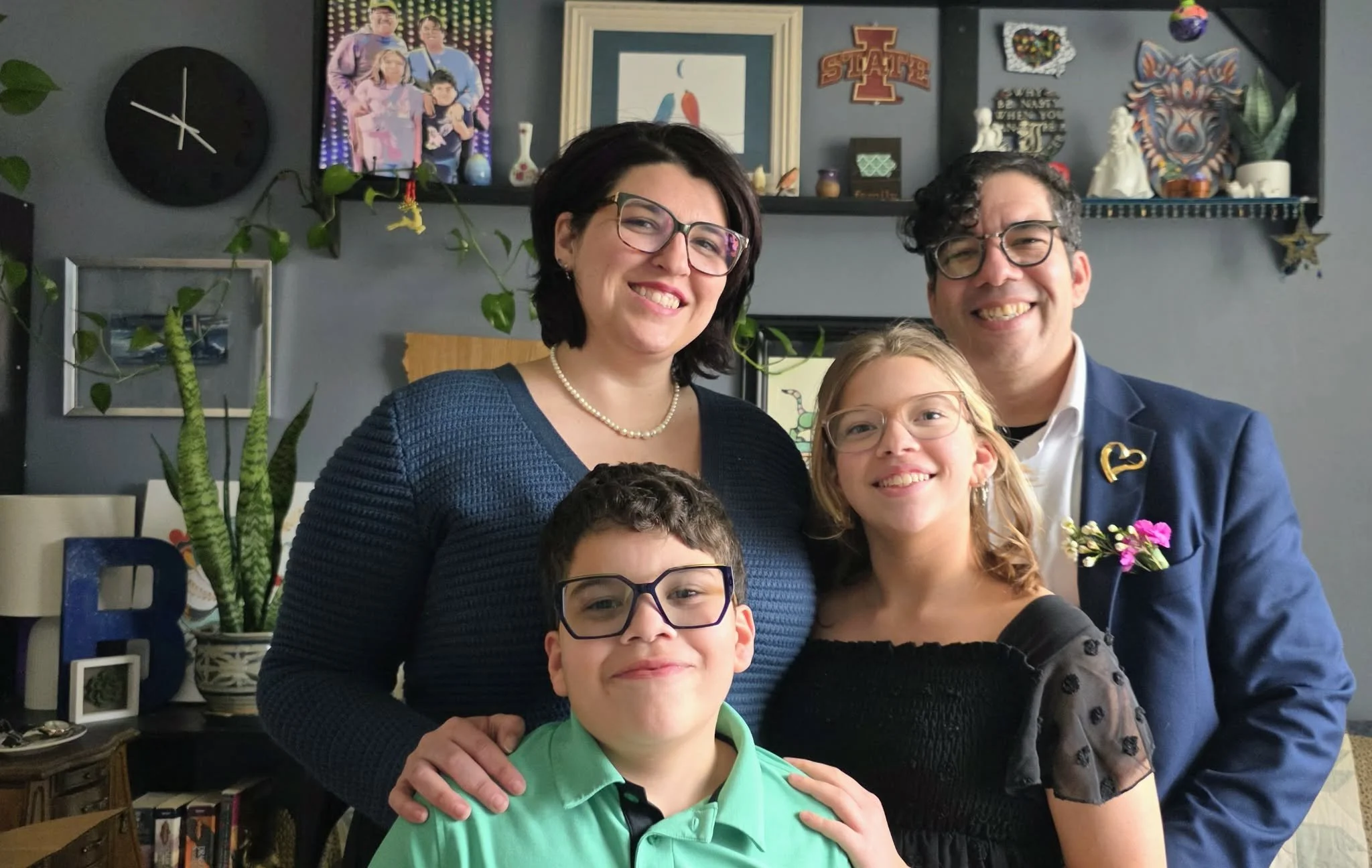 A family of four smiling and posing for a photo in a cozy living room.