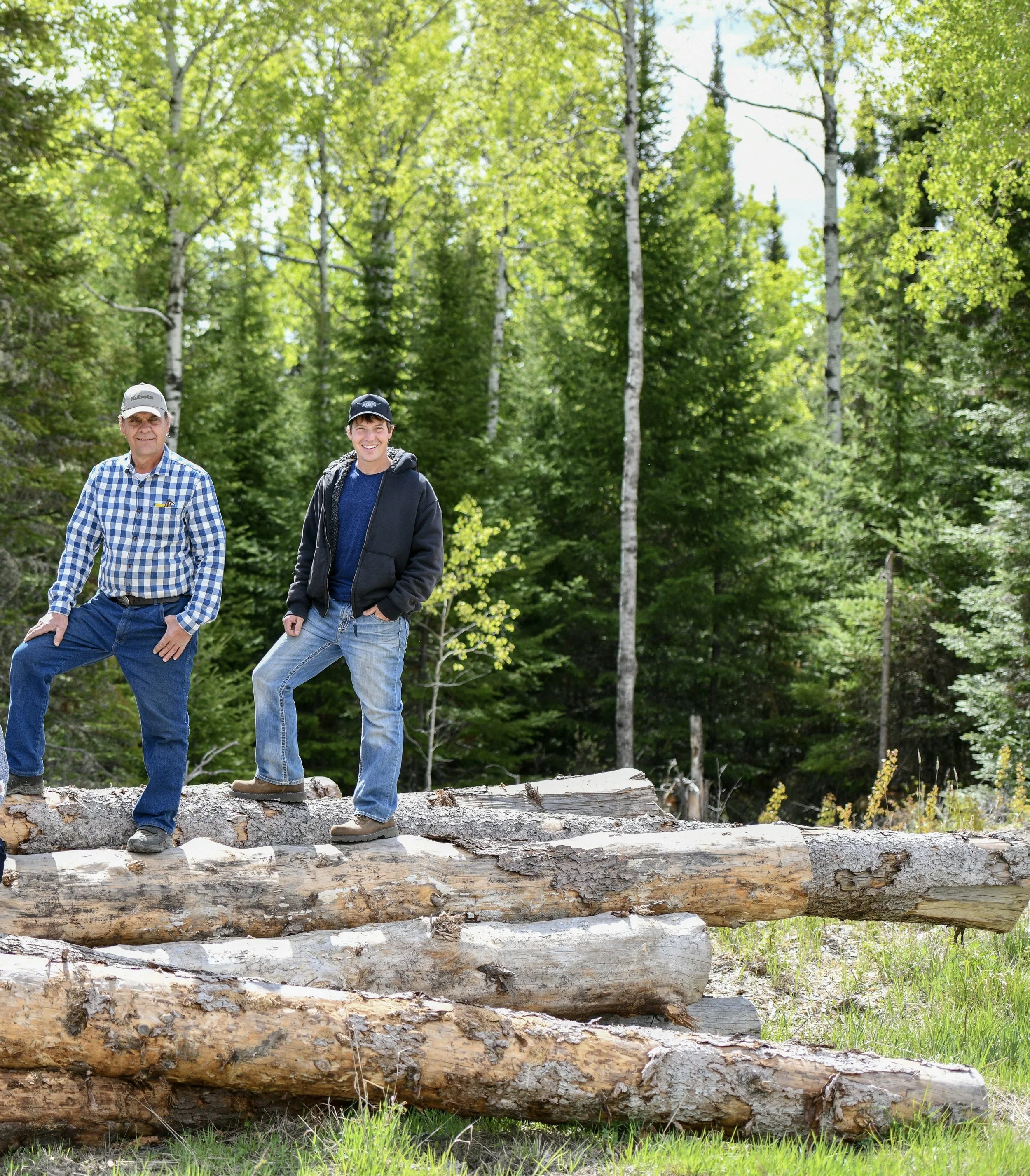 father and son owners stand on top a log pile at the sawmill