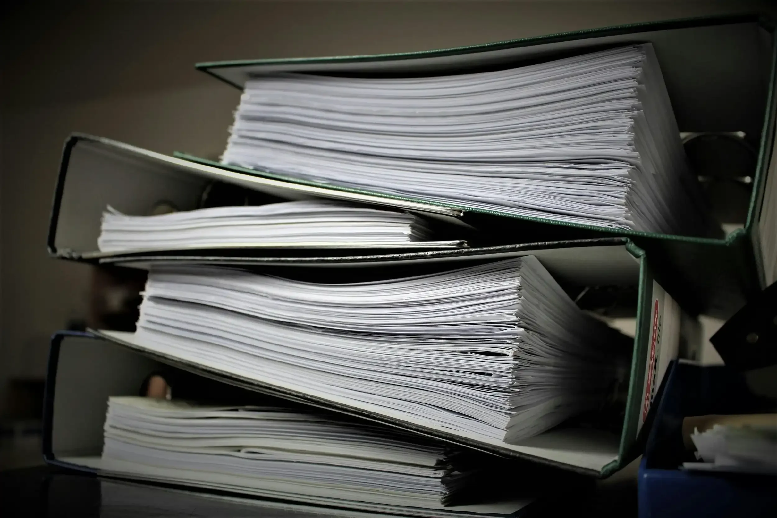 Four green metal file organizers filled with stacked white papers on a dark surface.