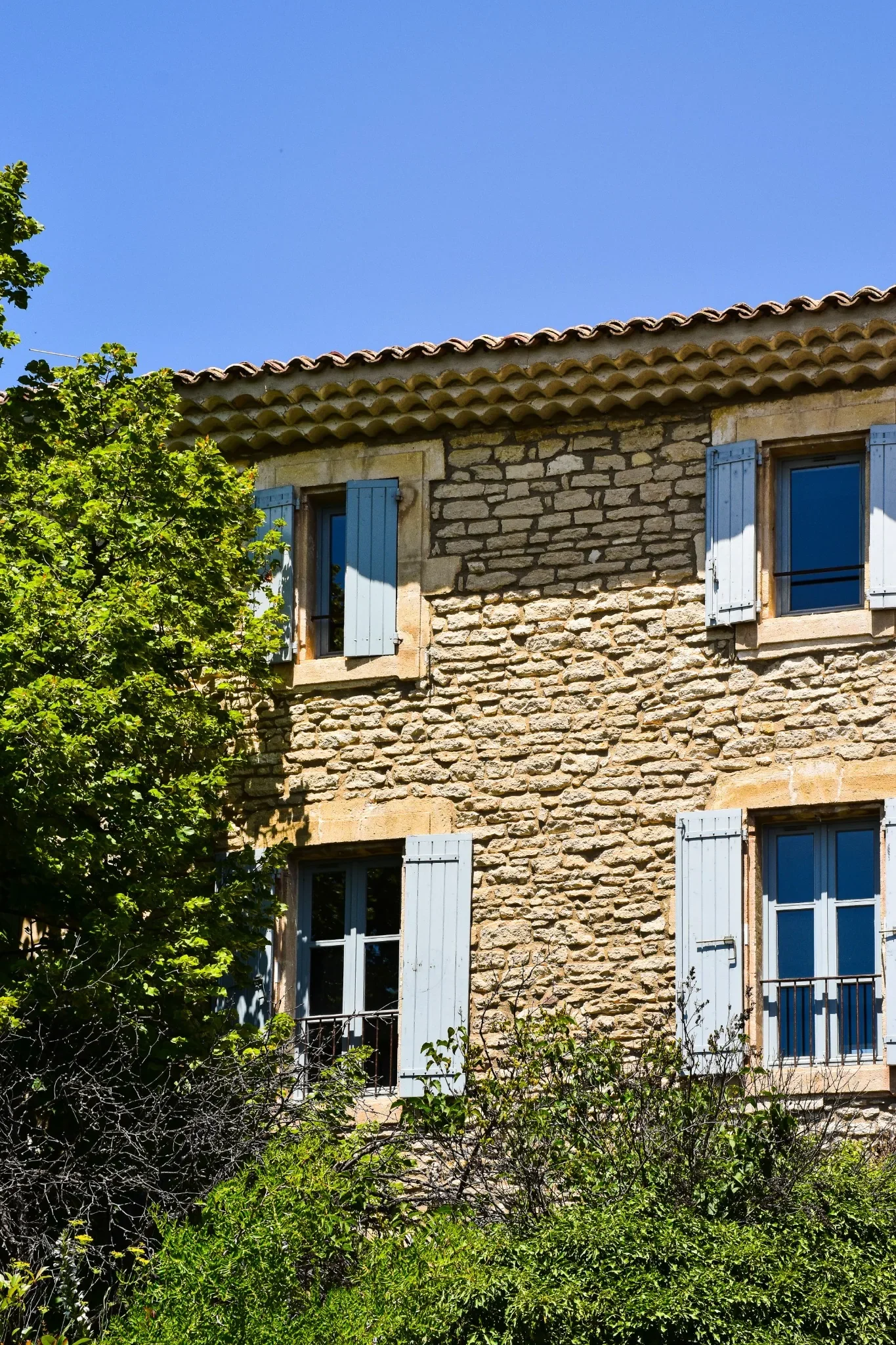 Façade d'une maison provençale en pierre avec volets bleus et jardin, illustrant une résidence secondaire dans le Sud de la France.