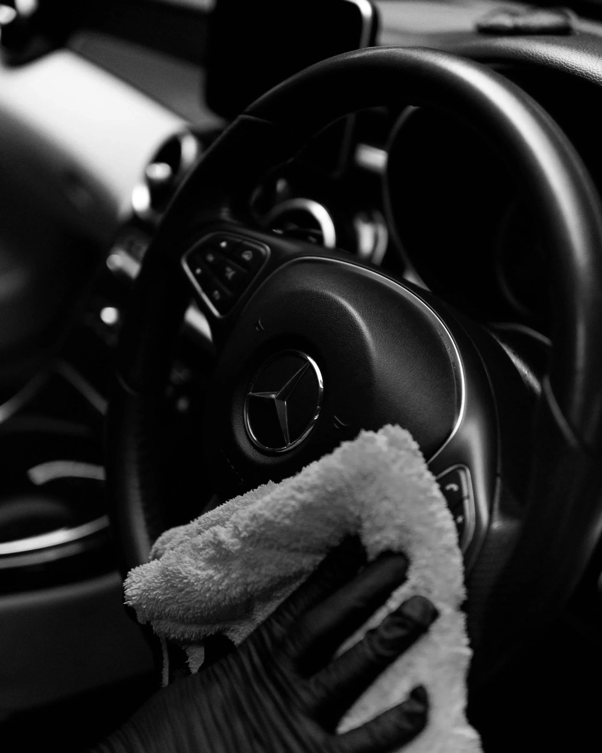 Innenraum eines Autos, Fokus auf das Lenkrad mit Mercedes-Logo, auf dem Armaturenbrett liegen Gegenstände, im Vordergrund ein weiches, graues Tuch oder Handtuch.