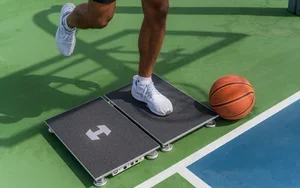 Person jumping onto a platform on a basketball court with a basketball nearby.