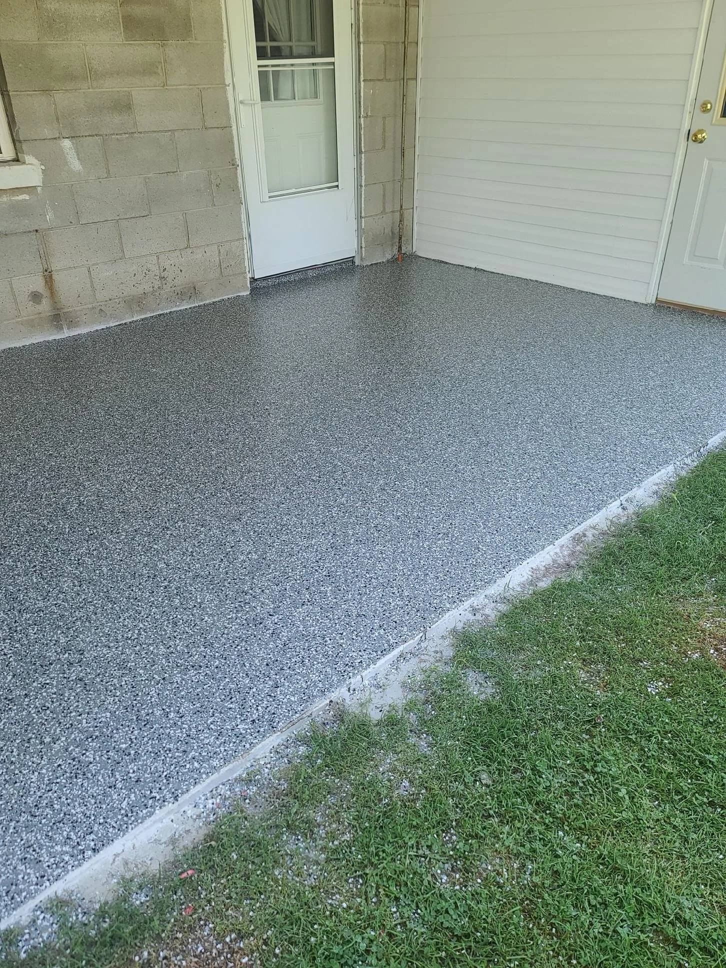 Newly poured concrete porch with a textured surface next to green grass.