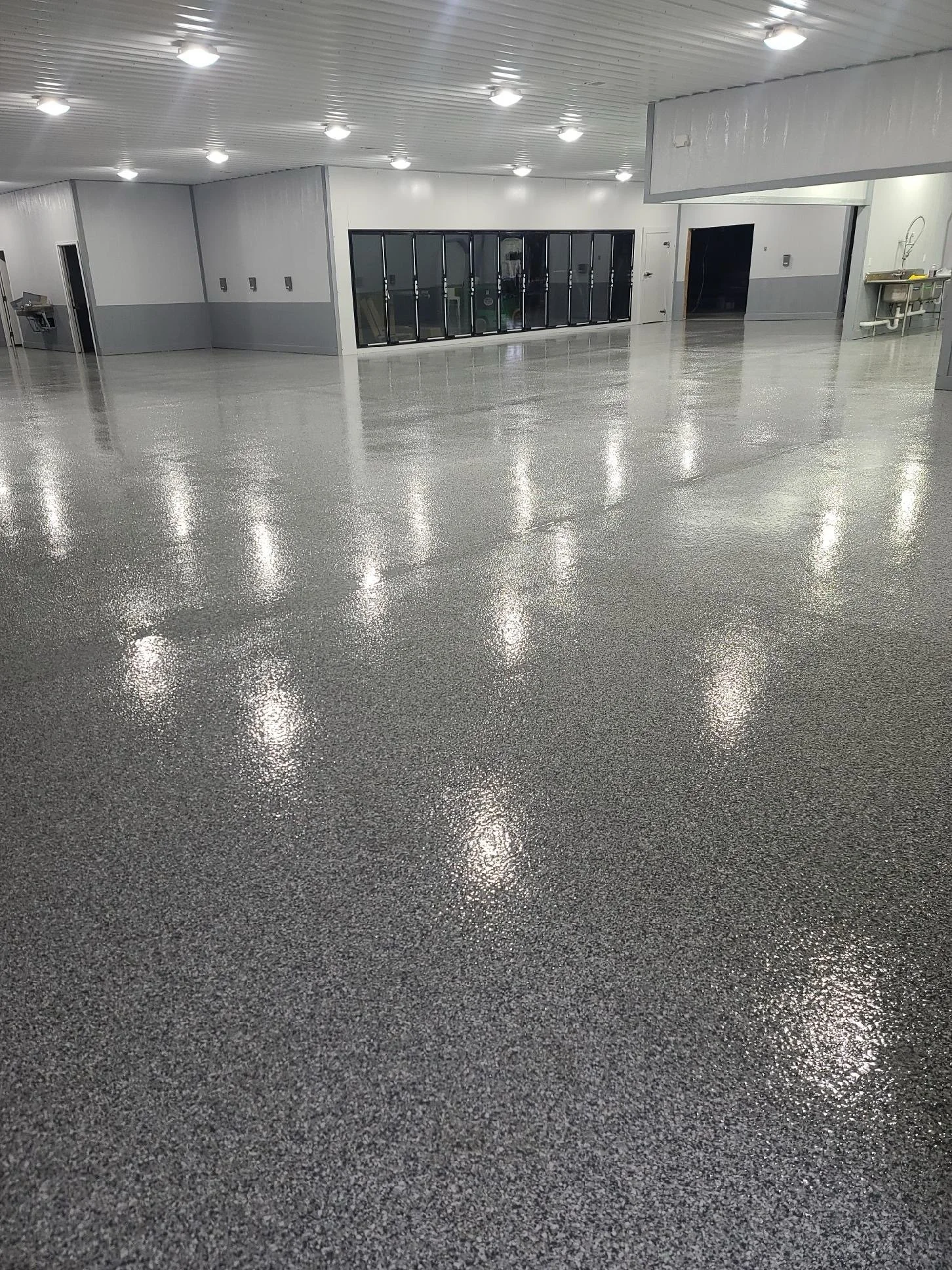 Empty commercial or industrial space with a shiny, speckled epoxy floor, white walls, and fluorescent ceiling lights.