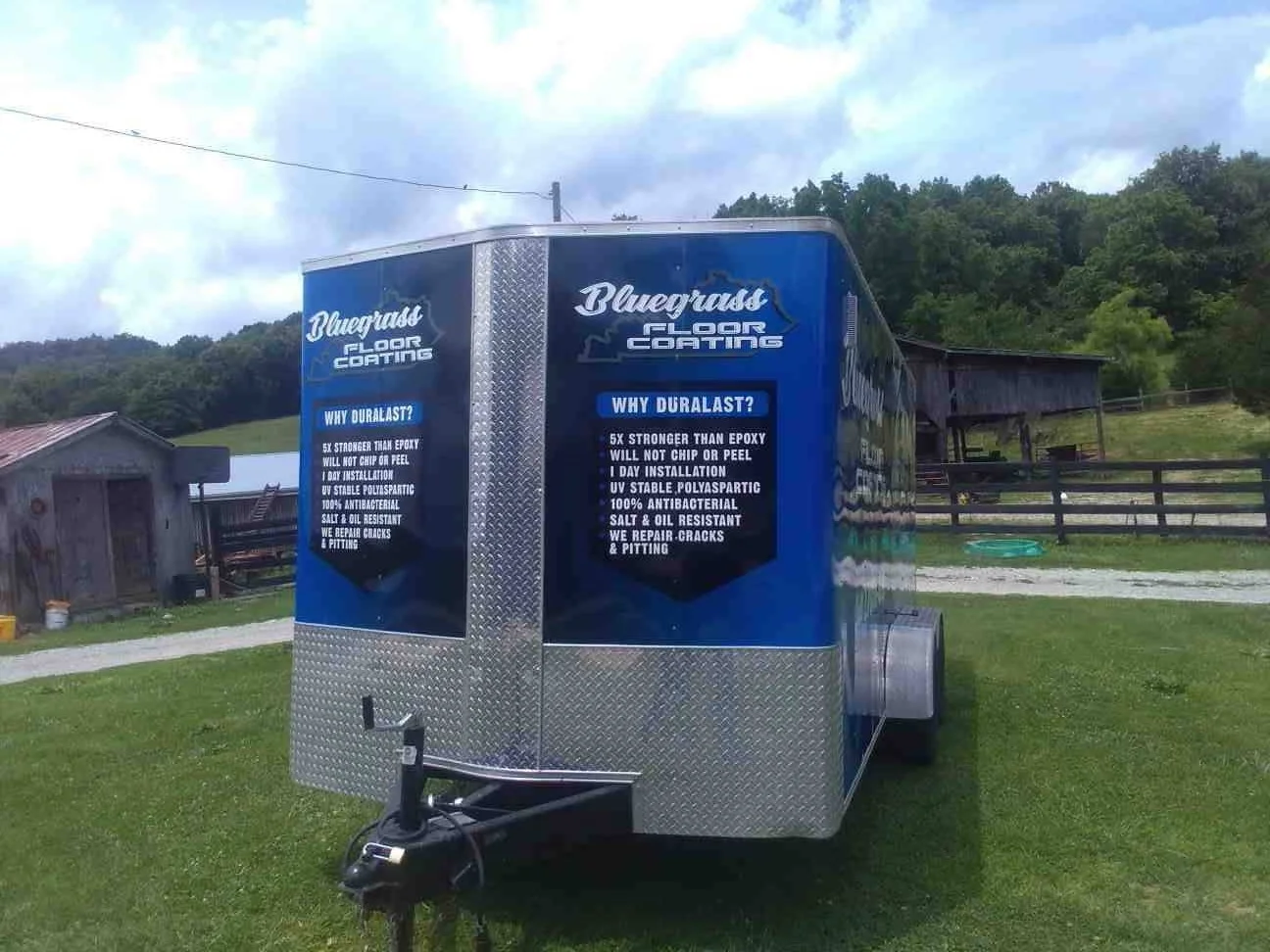 A blue trailer for Bluegrasp Floor Coating parked on a grassy area with trees and a barn in the background.