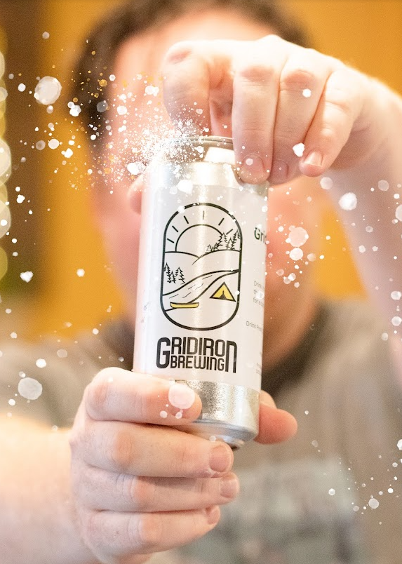 A person holding a can of Gridiron Brewing beer, with spray and foam around it.