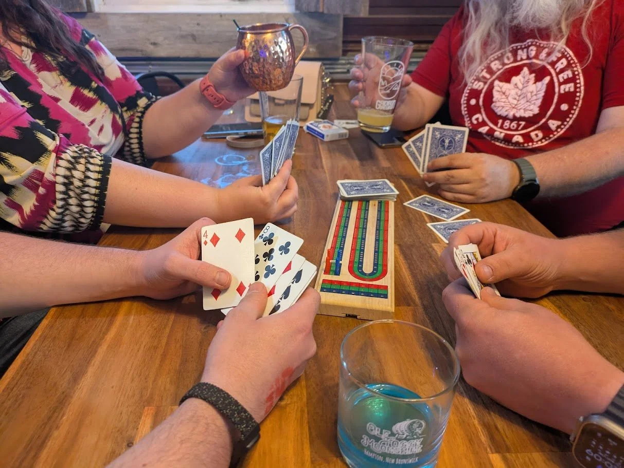 People playing a game of cards at a wooden table with drinks and a Snakes and Ladders game in the center.