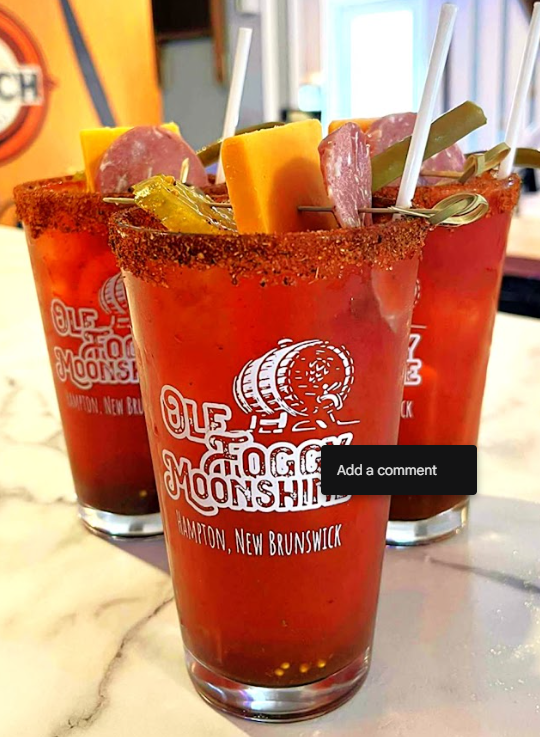 Three Bloody Mary cocktails garnished with celery, cheese, pepperoni, and pickles, on a marble countertop.