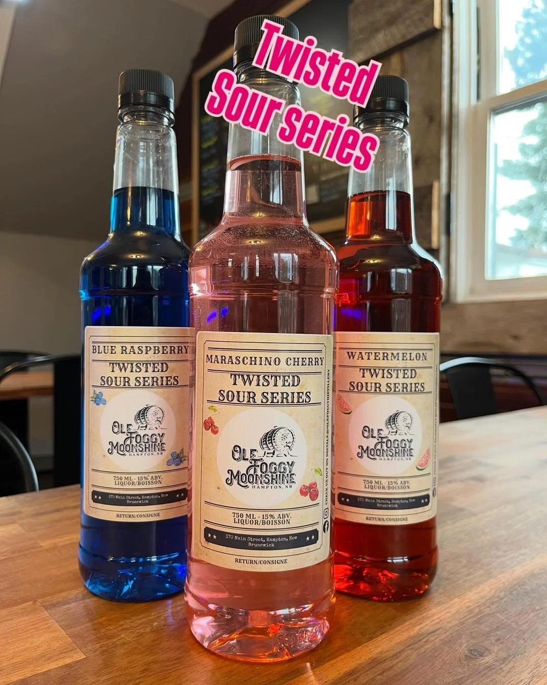 Three bottles of twisted sour series beverages with blue raspberry, maraschino cherry, and watermelon flavors, placed on a wooden table near a window.