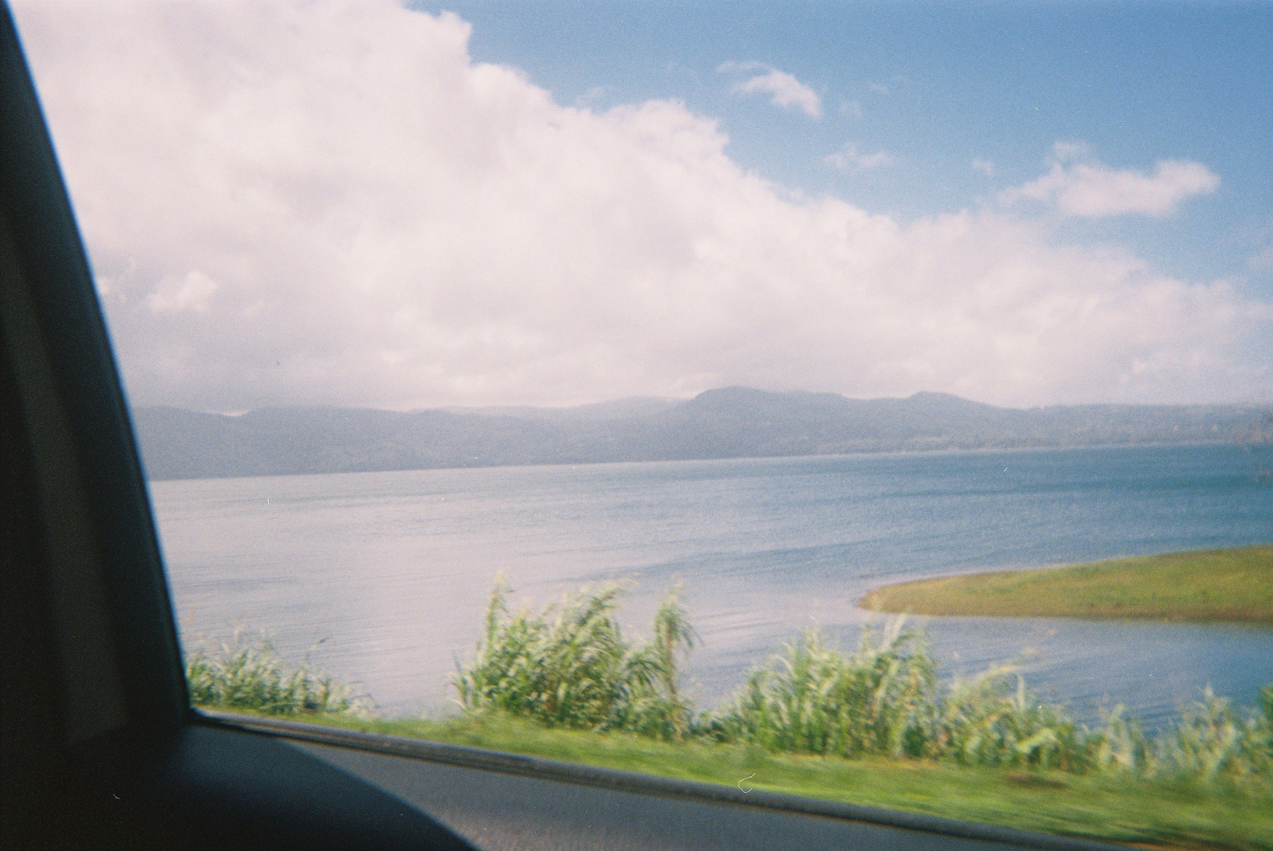 Scenic view of a lake with mountains in the distance, taken from inside a vehicle through the side window.