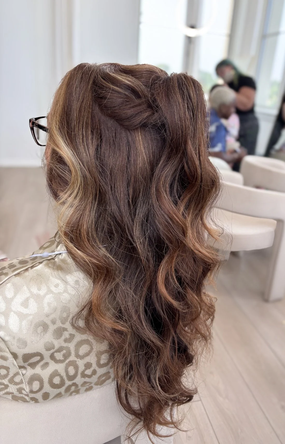 Side view of a woman with long, wavy, chestnut-colored hair in an indoor setting.