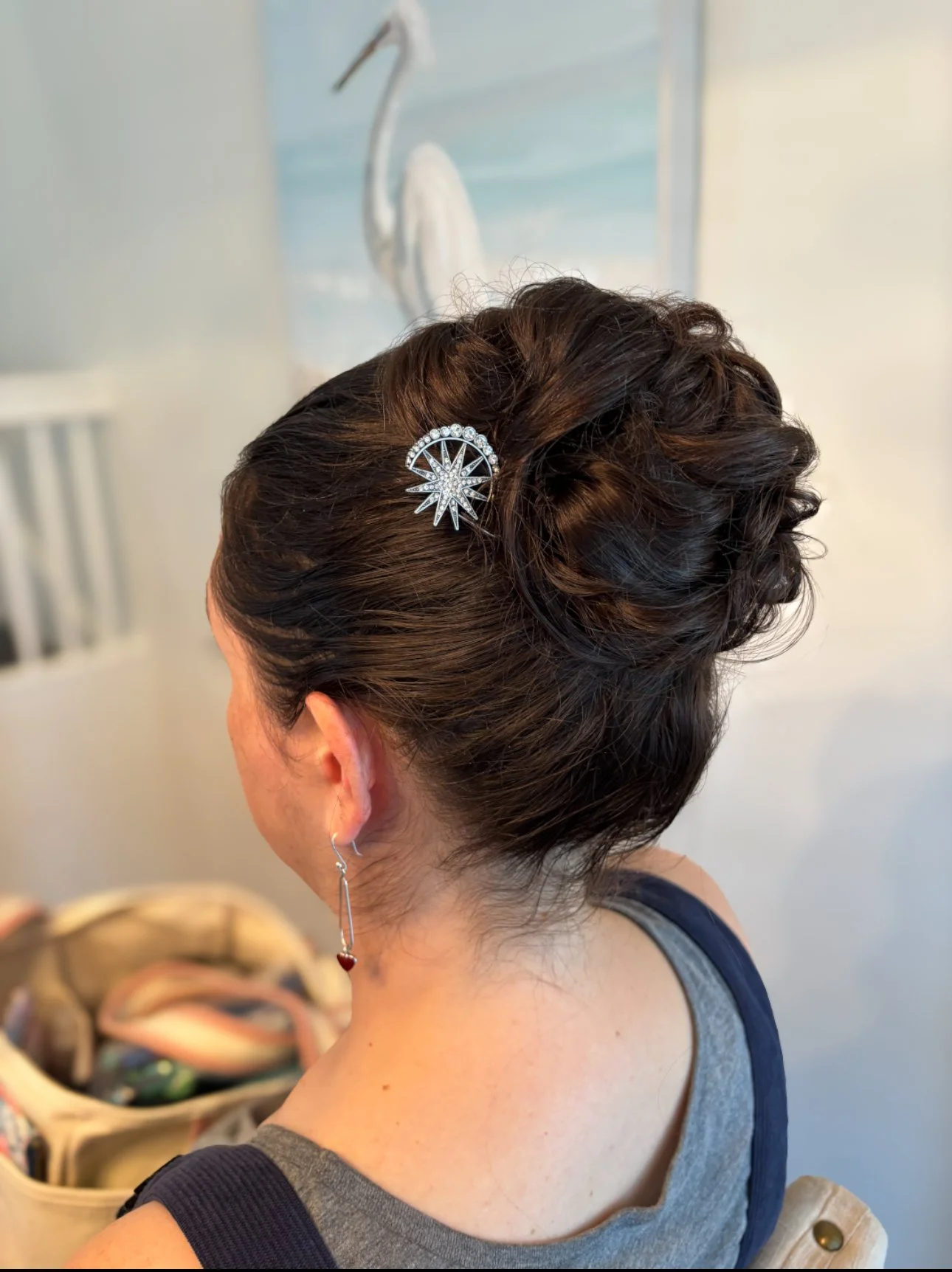 A woman with dark brown hair styled in an elegant updo, wearing a star-shaped hairpin with rhinestones, and silver earrings with a small red heart charm.