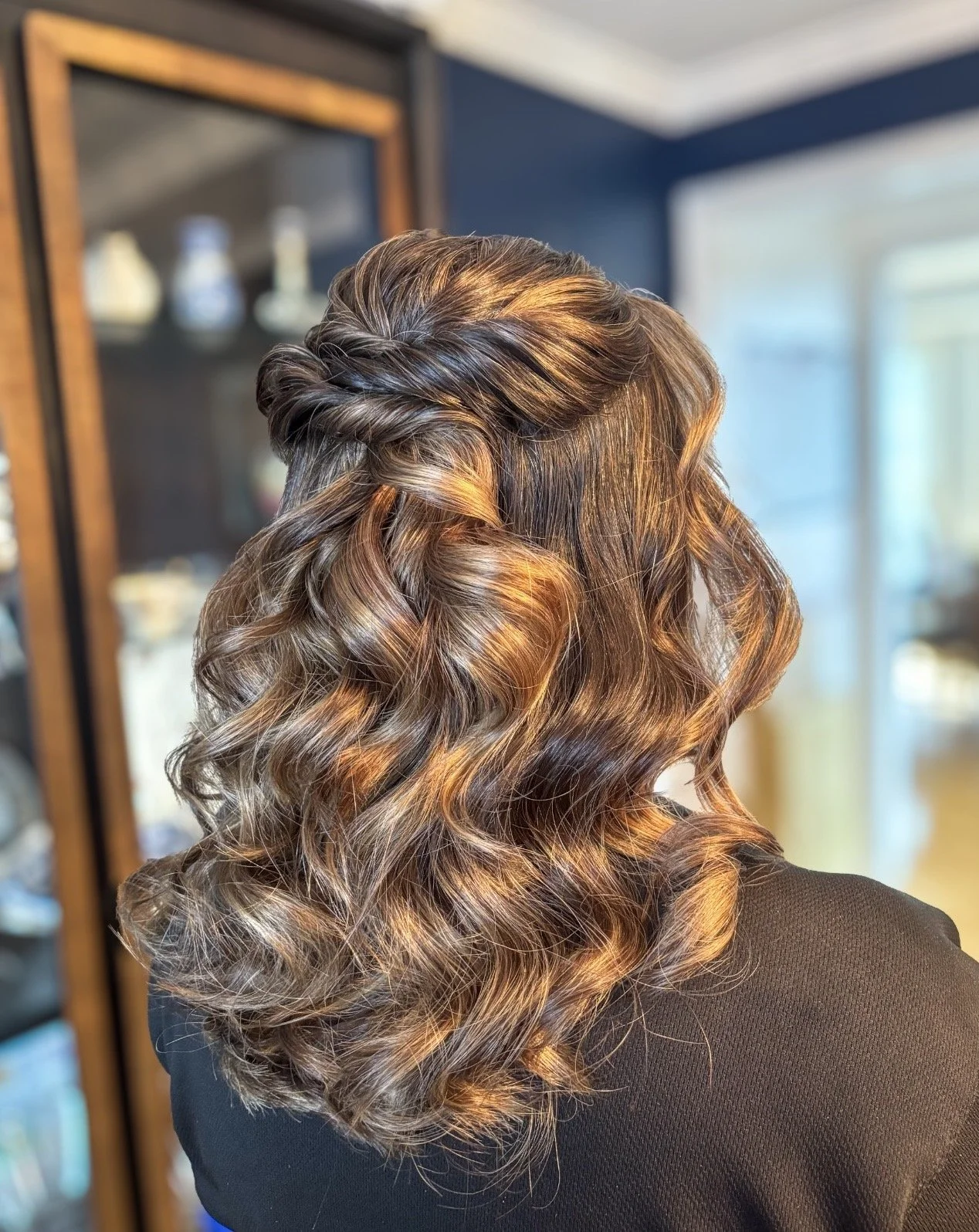 Back of a woman's head with shoulder-length, curly hair with caramel and dark brown highlights.