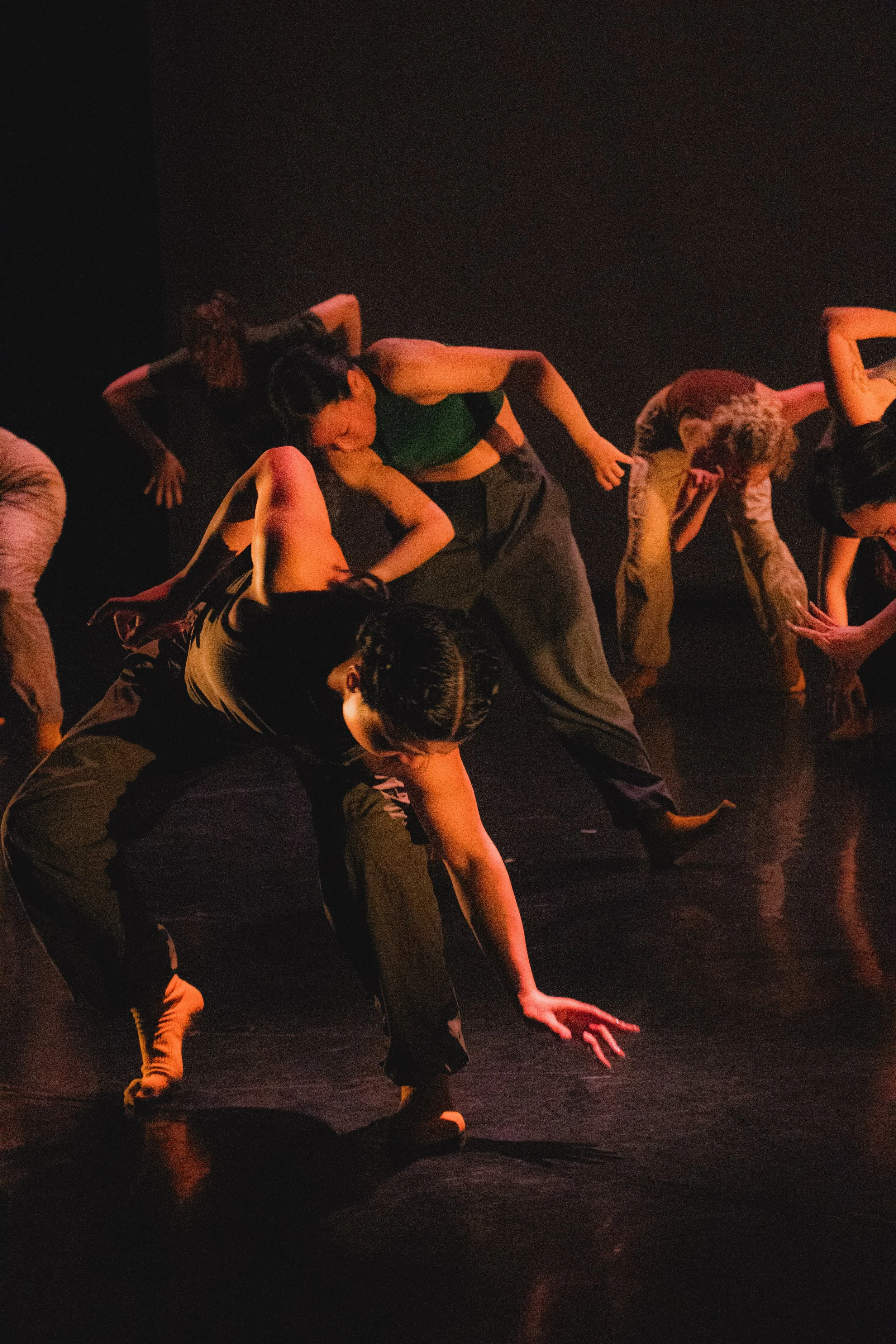 A group of dancers performing on stage in low lighting, wearing casual dark clothing, and in various dynamic poses.