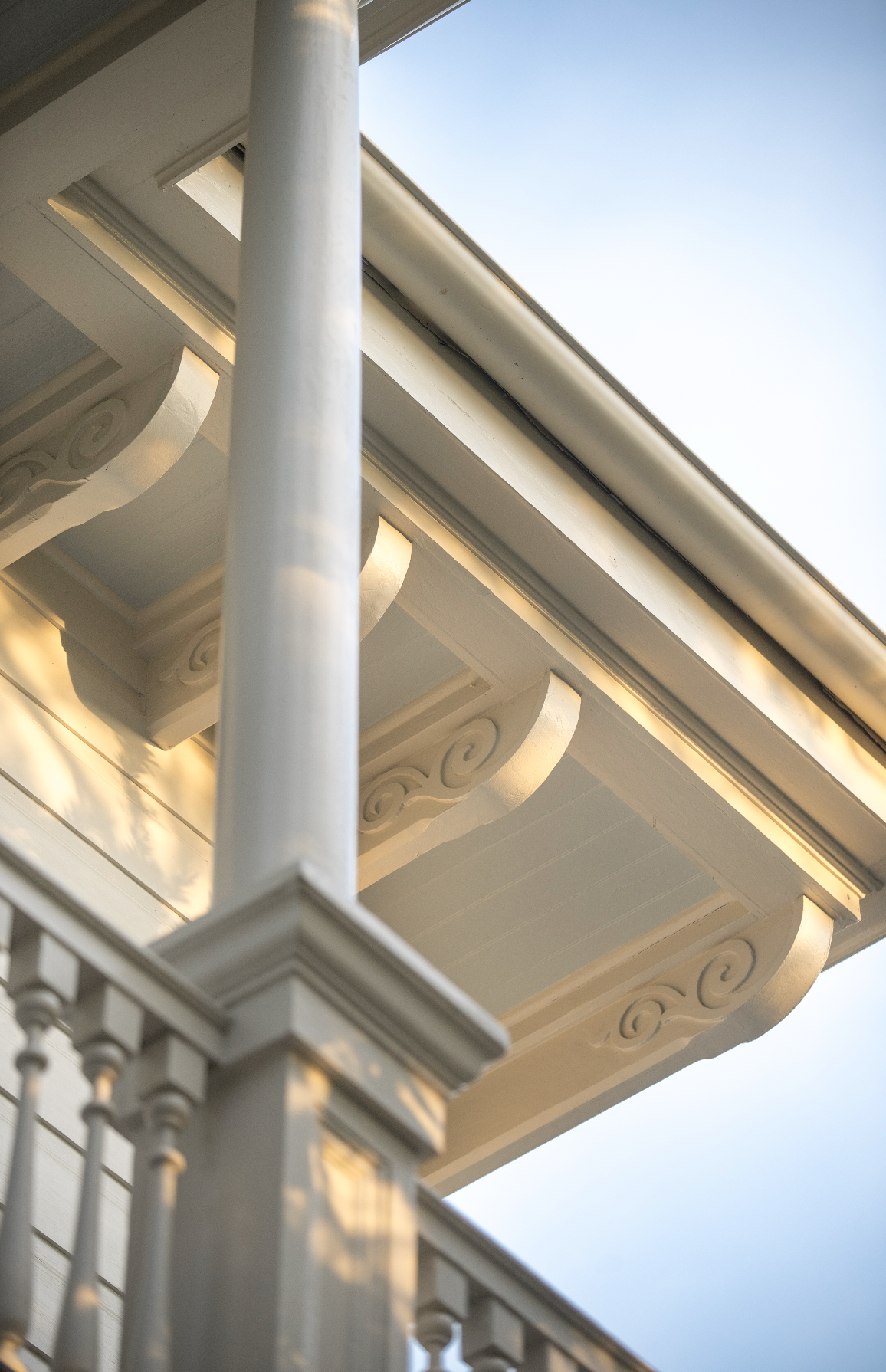 Close-up of a house's ornate white porch railing and decorative trim, with a clear blue sky in the background.