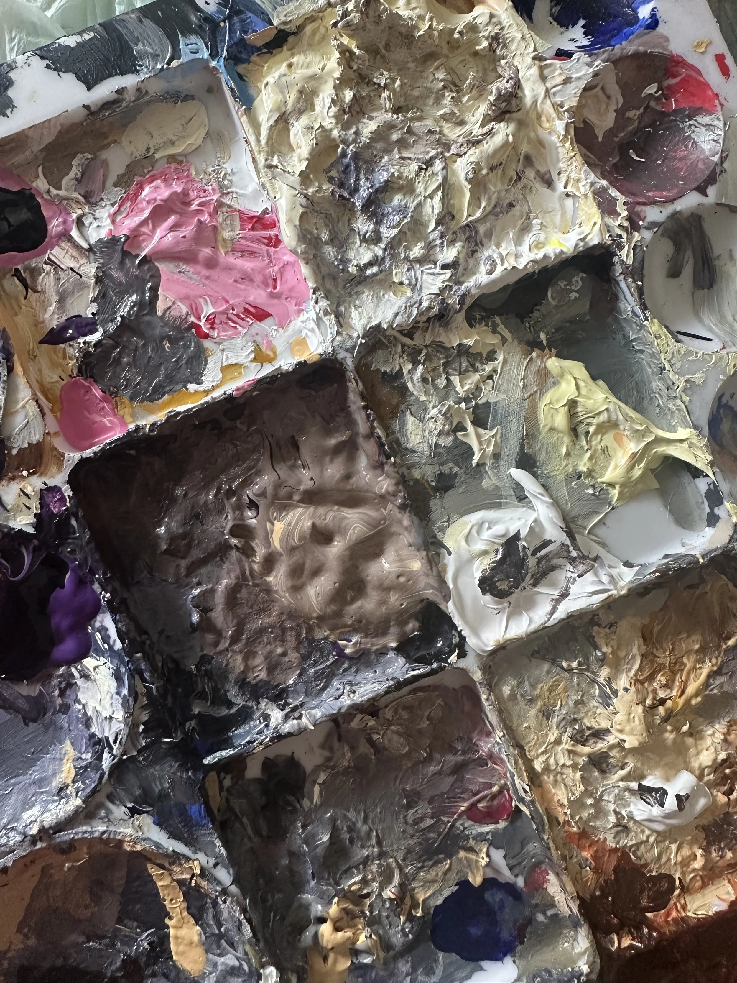 A close-up view of artist's oil paints and mixing palette with various colors and textures.