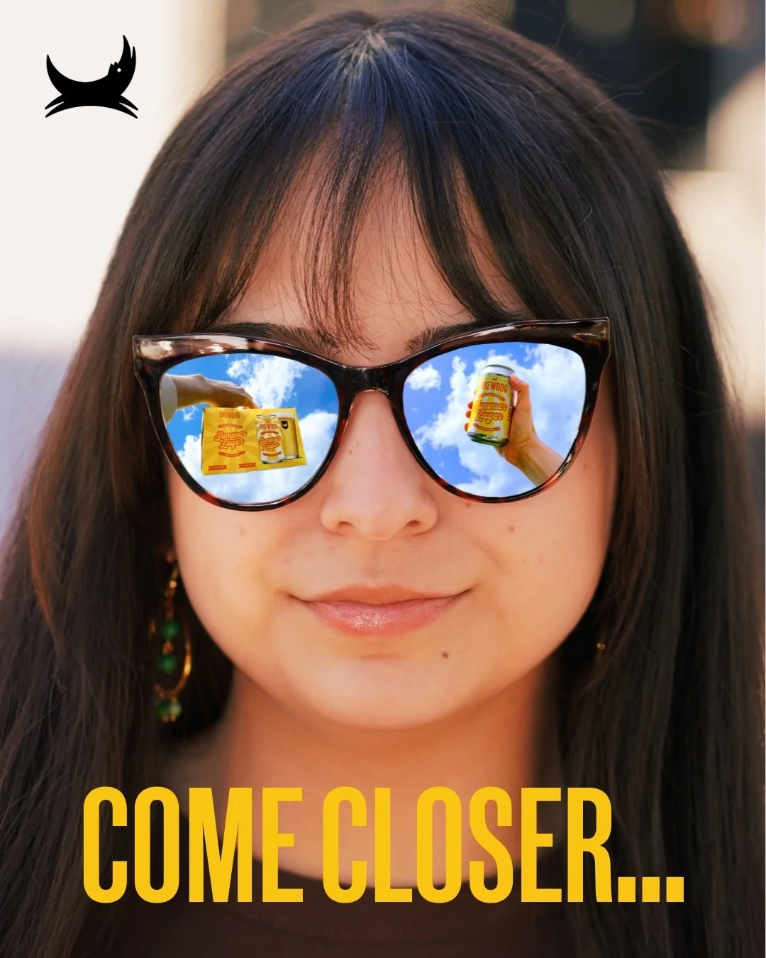 A woman wearing sunglasses with reflections of a yellow soda can and a beverage container, displaying a blue sky with clouds. Text at the bottom says 'COME CLOSER...'.