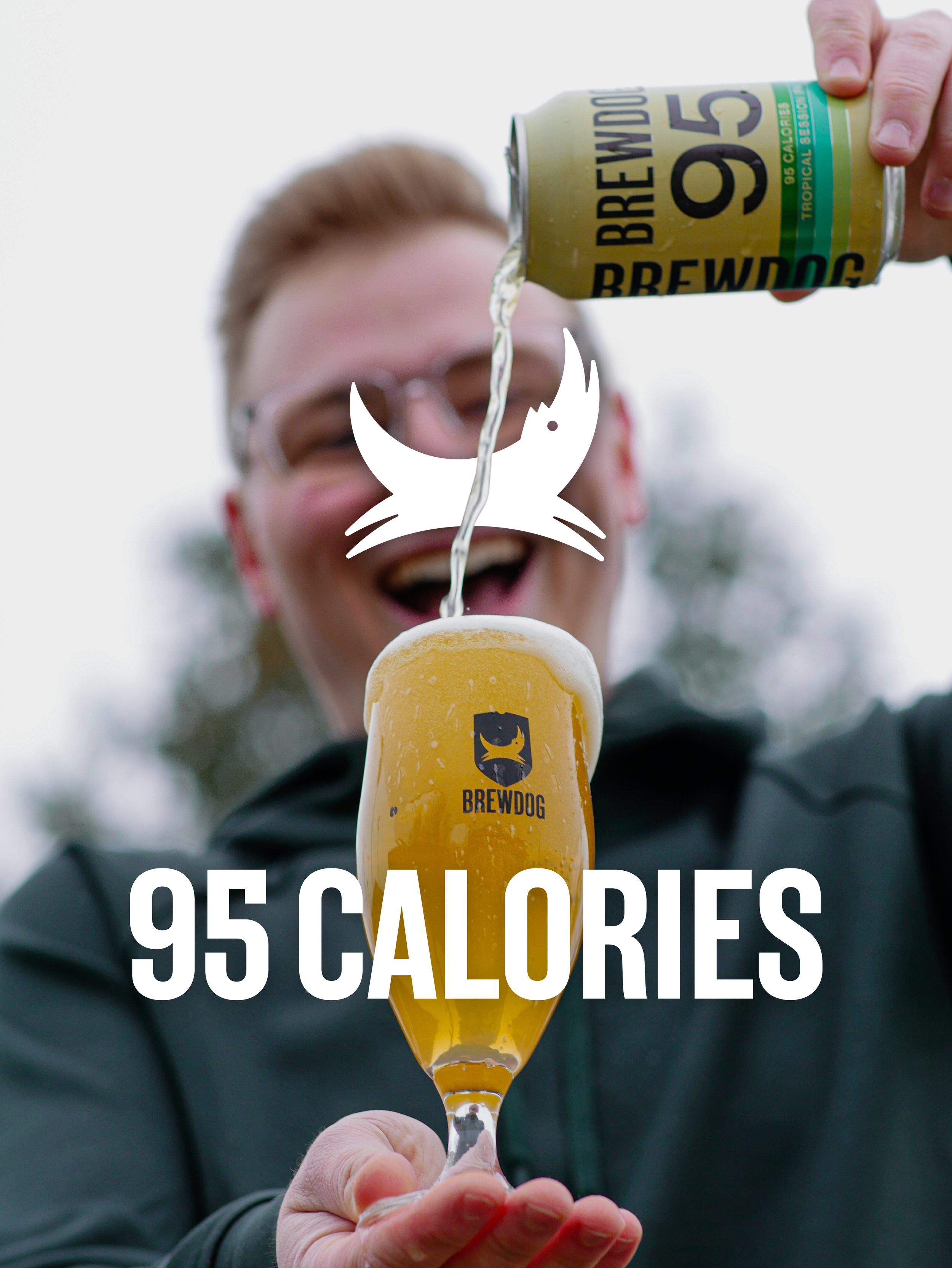 A person holding a glass of beer with a Brewdog branding, pouring beer from a Brewdog can labeled 95 calories. The background is blurred.