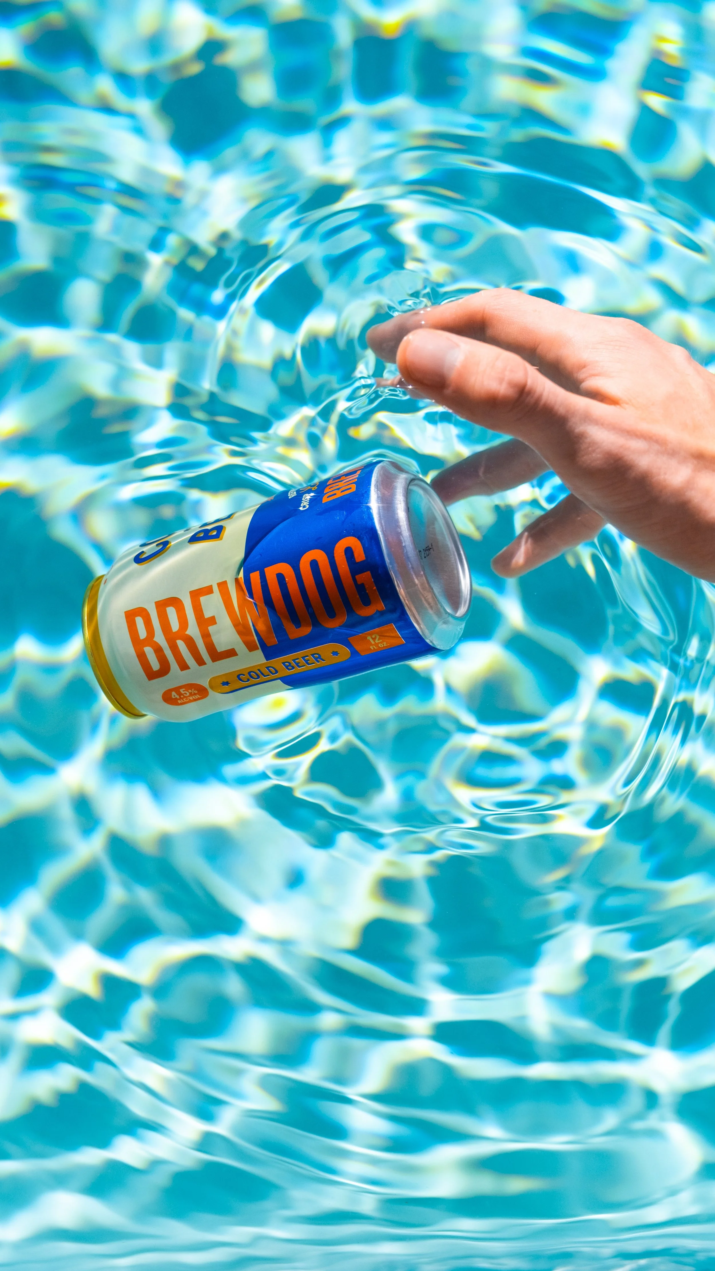 Can of brew dog beer floating on water in swimming pool, hand reaching towards it.