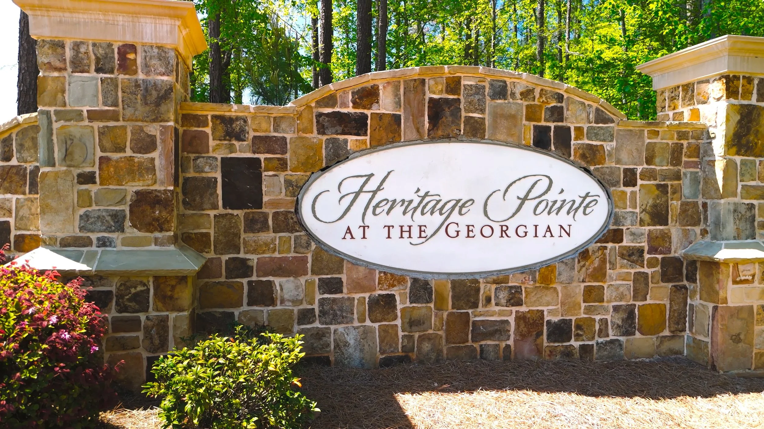 Stone entrance sign reading 'Heritage Pointe at the Georgian' surrounded by greenery and flowers.