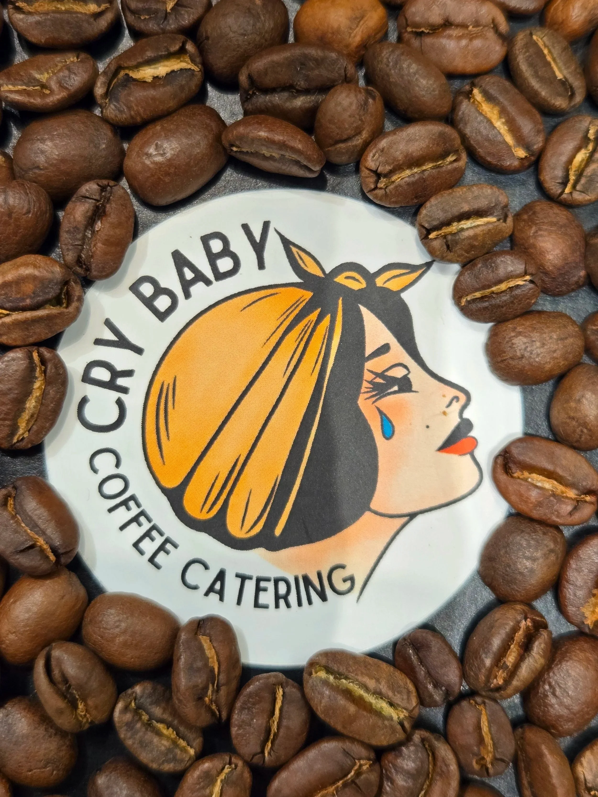 Cry Baby Coffee Catering Logo among Coffee Beans.