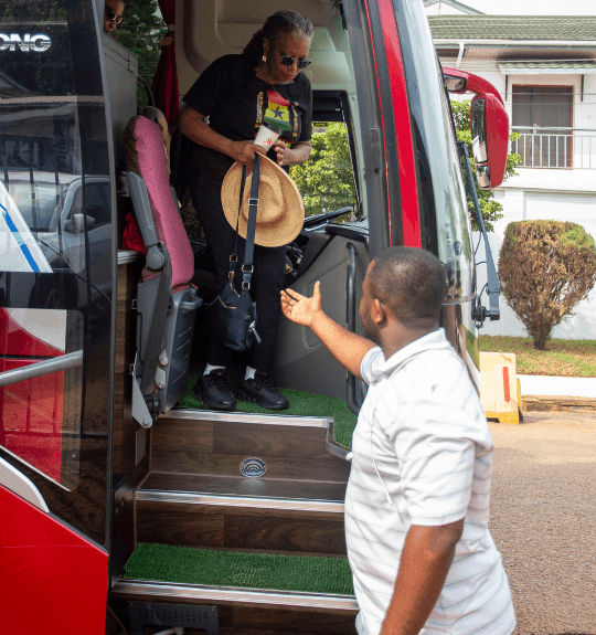 A Ghanaian local guide with his hand stretched out to help a tour guest get down a bus