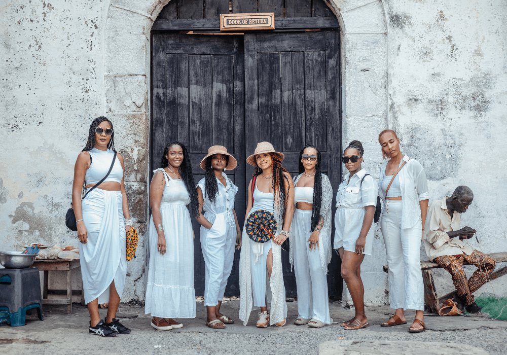 Seven women in white outfits standing in front of the  'Door of Return' at the Cape Coast Castle in Ghana