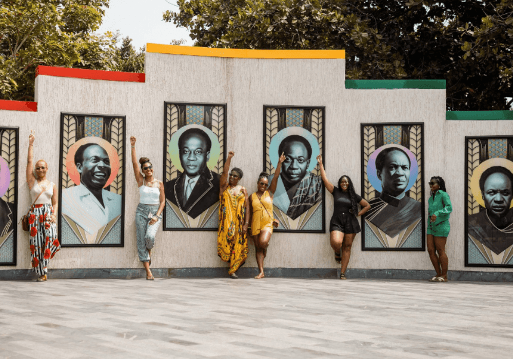 6 women with their hands in the air happily taking  a picture with portraits of Kwame Nkrumah during  atrip to Ghana